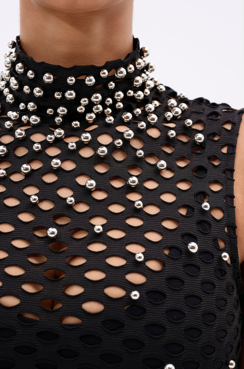 A close-up of someone wearing the METAL ORB DISTRESSED SLEEVELESS TOP, featuring a black textured finish with oval cutouts and silver bead details around the high neckline and chest.