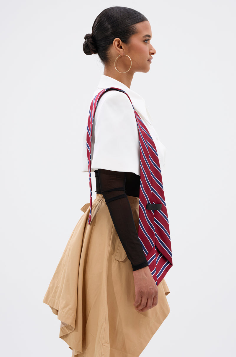 A woman in profile wears the GET WITH IT BUTTON DOWN BODYSUIT, styled with a red striped tie over her shoulder, a tan layered skirt, sheer off-the-shoulder sleeves, large hoop earrings, and her hair in a bun.
