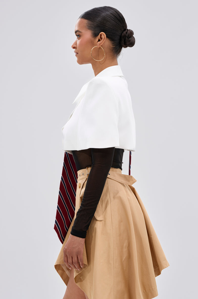 A woman in profile wears the GET WITH IT BUTTON DOWN BODYSUIT with a red striped tie, beige asymmetrical skirt, and large hoop earrings. Her hair is in a low bun and she stands against a plain gray background.