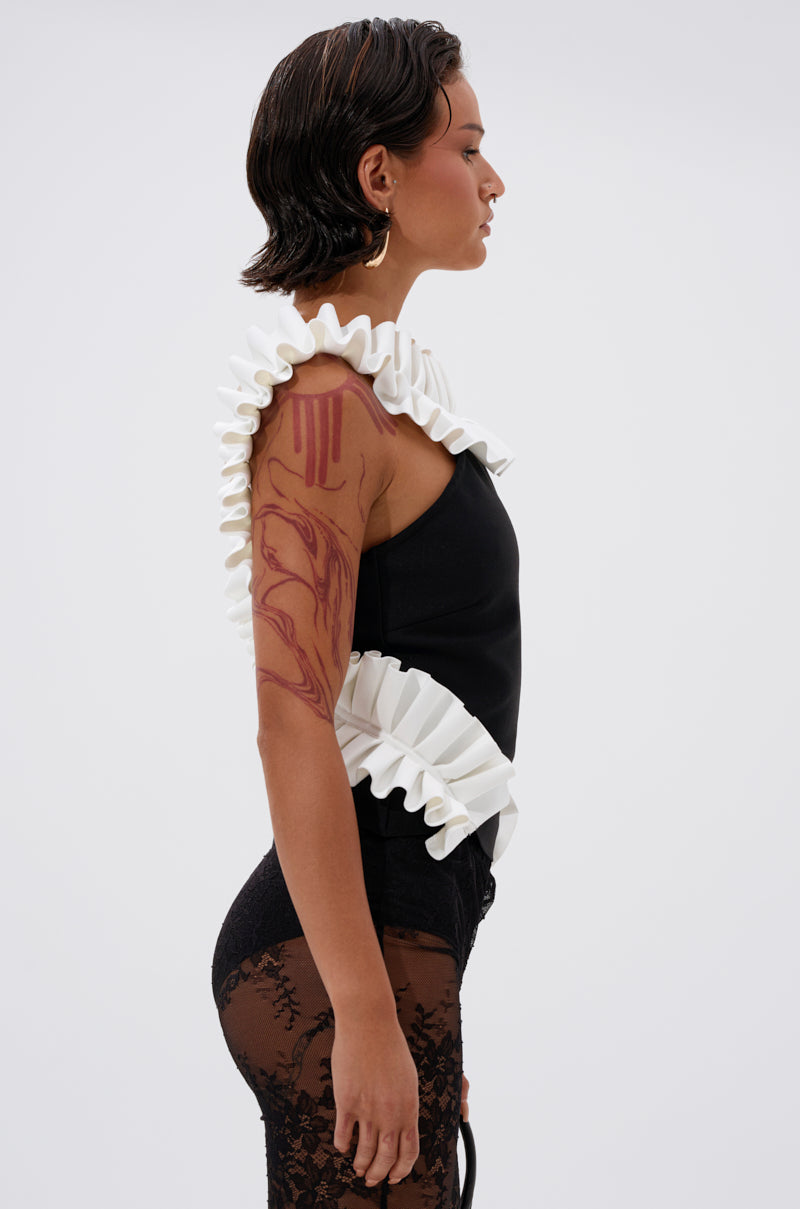 A woman with short dark hair stands in profile, wearing the BAROQUE MOCK NECK TOP paired with sheer black lace pants, visible tattoos, and a small black bag for a standout vintage-inspired look. 2