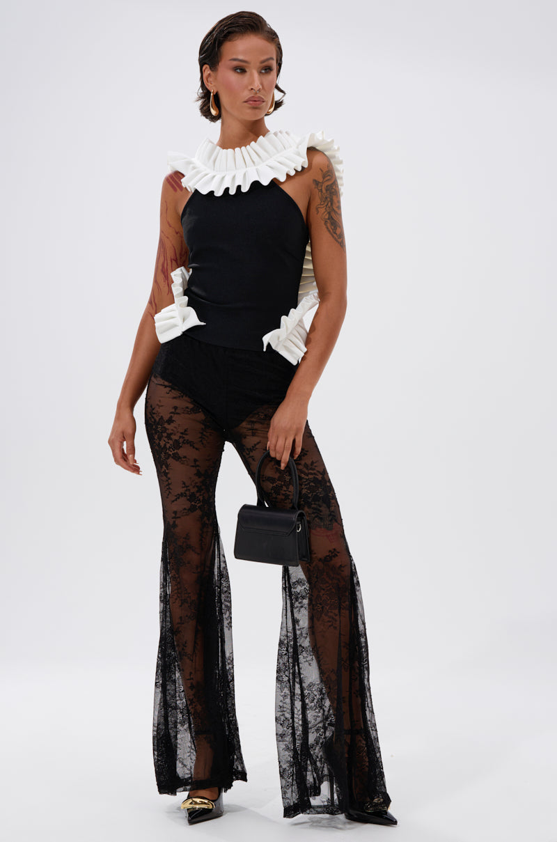 A person poses in the BAROQUE MOCK NECK TOP with dramatic white ruffles, high-waisted sheer black lace pants, gold pointed shoes, and a small black handbag against a plain white background. 5