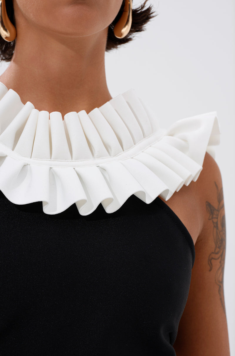 A close-up of a person wearing the BAROQUE MOCK NECK TOP, which features a large white pleated ruffle collar. They accessorize with gold hoop earrings and display a tattoo on their upper arm for an elegant yet bold look. 6