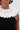 A close-up of a person wearing the BAROQUE MOCK NECK TOP, which features a large white pleated ruffle collar. They accessorize with gold hoop earrings and display a tattoo on their upper arm for an elegant yet bold look.