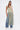 A woman wears the TIED DOWN V-NECK ROPE TOP featuring multicolored braided rope strands, styled with blue wide-leg jeans and white heels, standing against a plain white background.