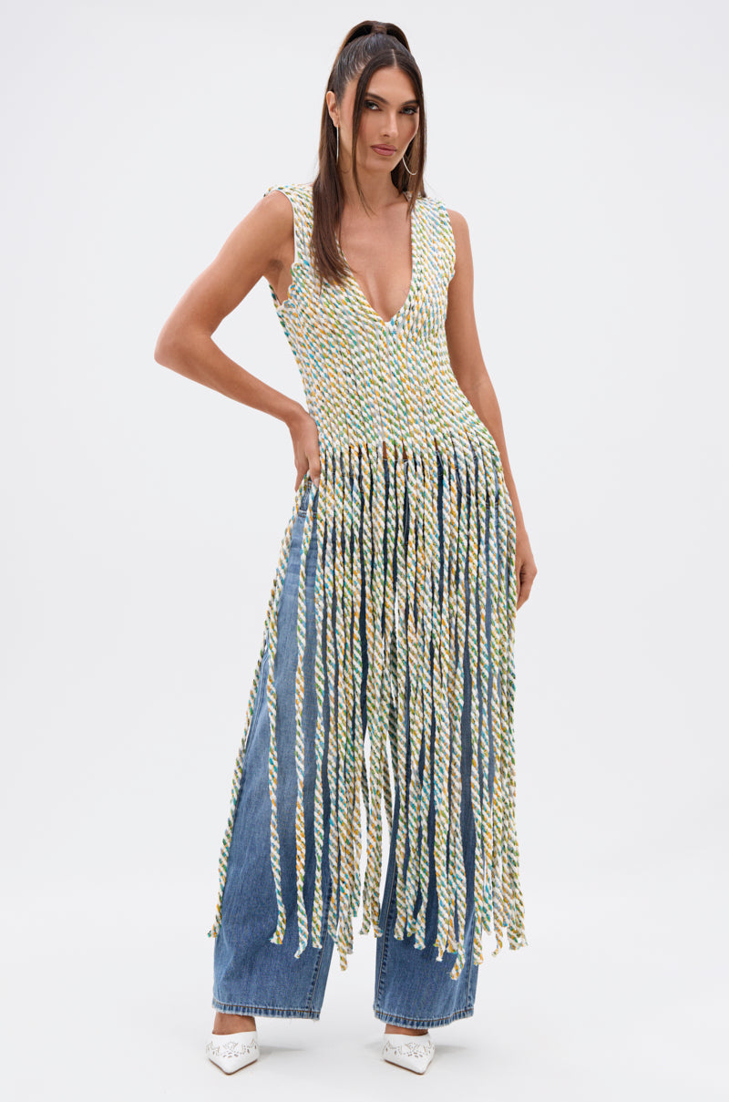 A woman poses in the TIED DOWN V-NECK ROPE TOP, a sleeveless design with colorful twisted cords, styled with wide-leg blue jeans and white pointed heels against a plain white background.
