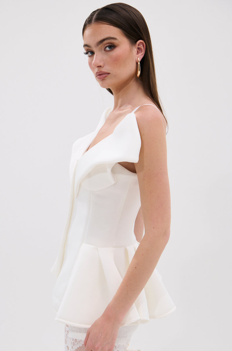 A woman with long brown hair models the DANCE AROUND SLEEVELESS PEPLUM CORSET, featuring a sculptural peplum hem. She poses sideways, looking at the camera against a plain white background. 2
