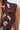 A close-up of a person wearing the SO BLESSED COWL NECK BLOUSE, a cropped sleeveless top decorated with silver pins, brooches, turquoise stones, and Western-themed circular, floral, and gun-shaped charms.