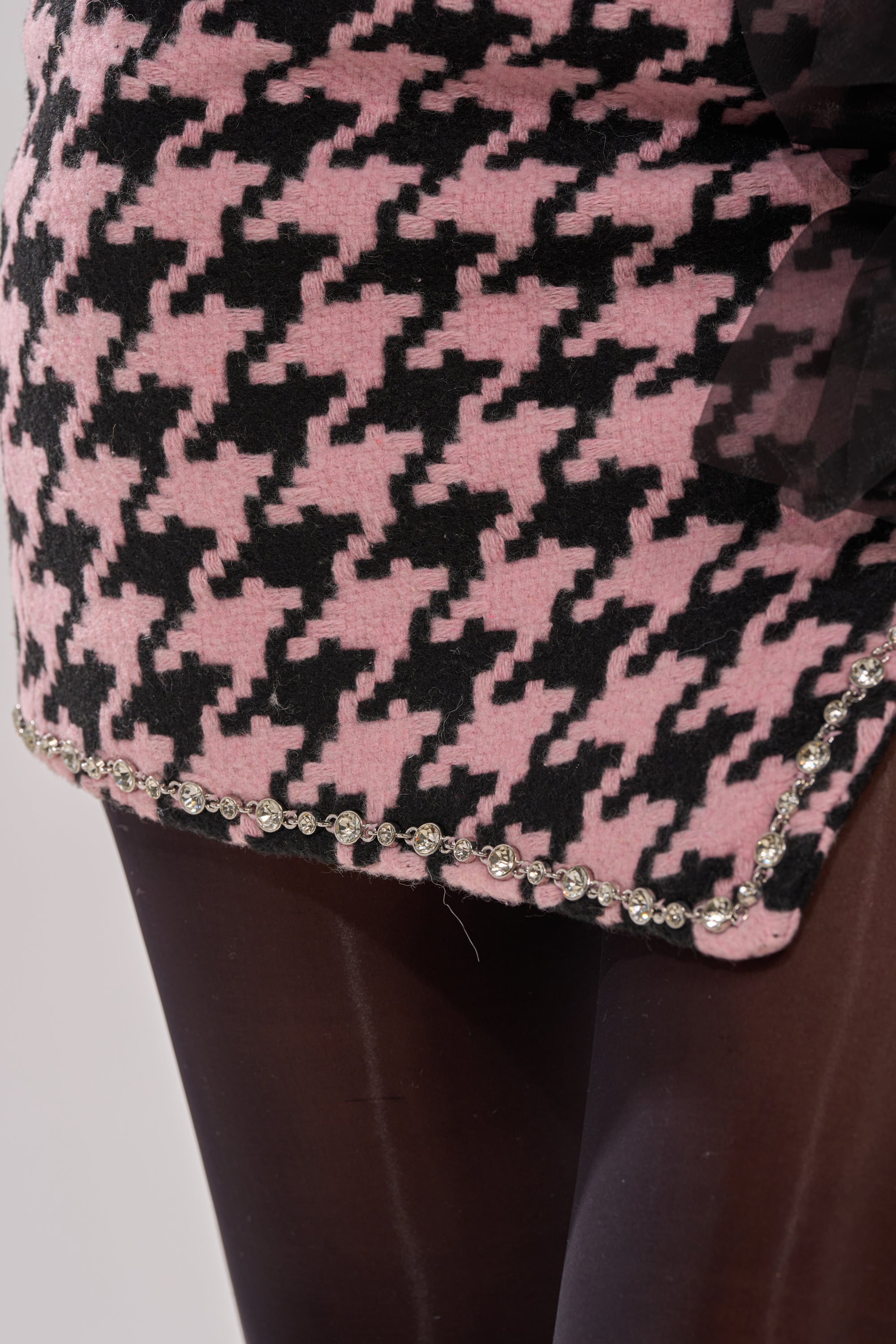 A close-up of the SMOOTH TRANSITION MINI SKIRT, featuring pink and black houndstooth, crystal-embellished beaded hem, styled over sheer black tights. 9