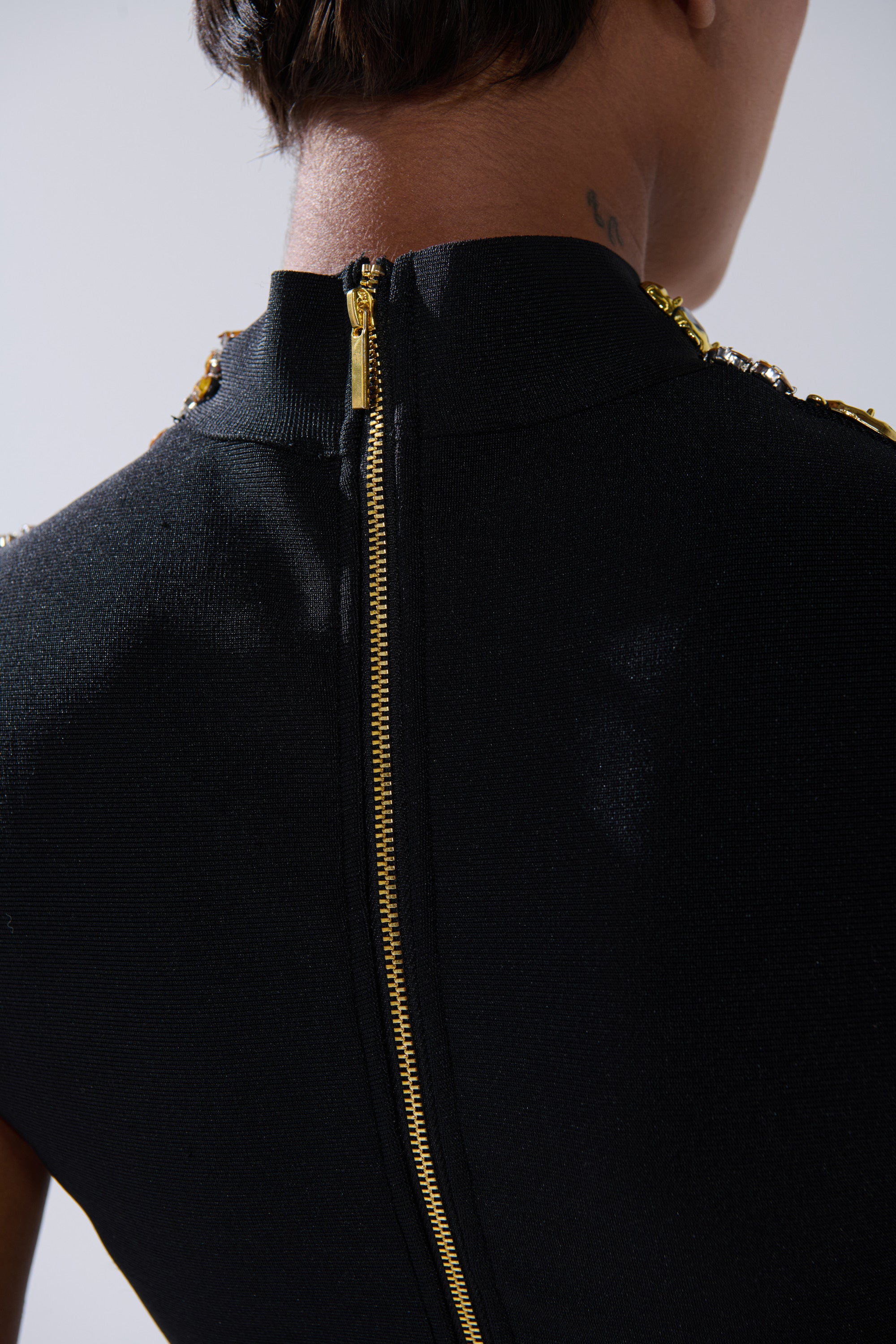 Close-up of the upper back and neck shows a GOLDEN GLAM BLOUSE with a visible gold zipper down the center. The photo highlights the blouse's back and part of the model's short hair.
