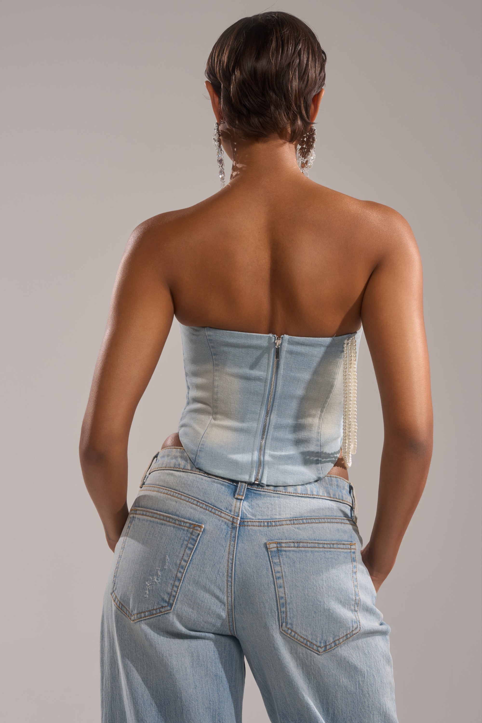 A person with short hair is shown from the back, wearing the PEARL QUEEN DENIM CORSET and matching denim jeans, standing against a plain light gray background.