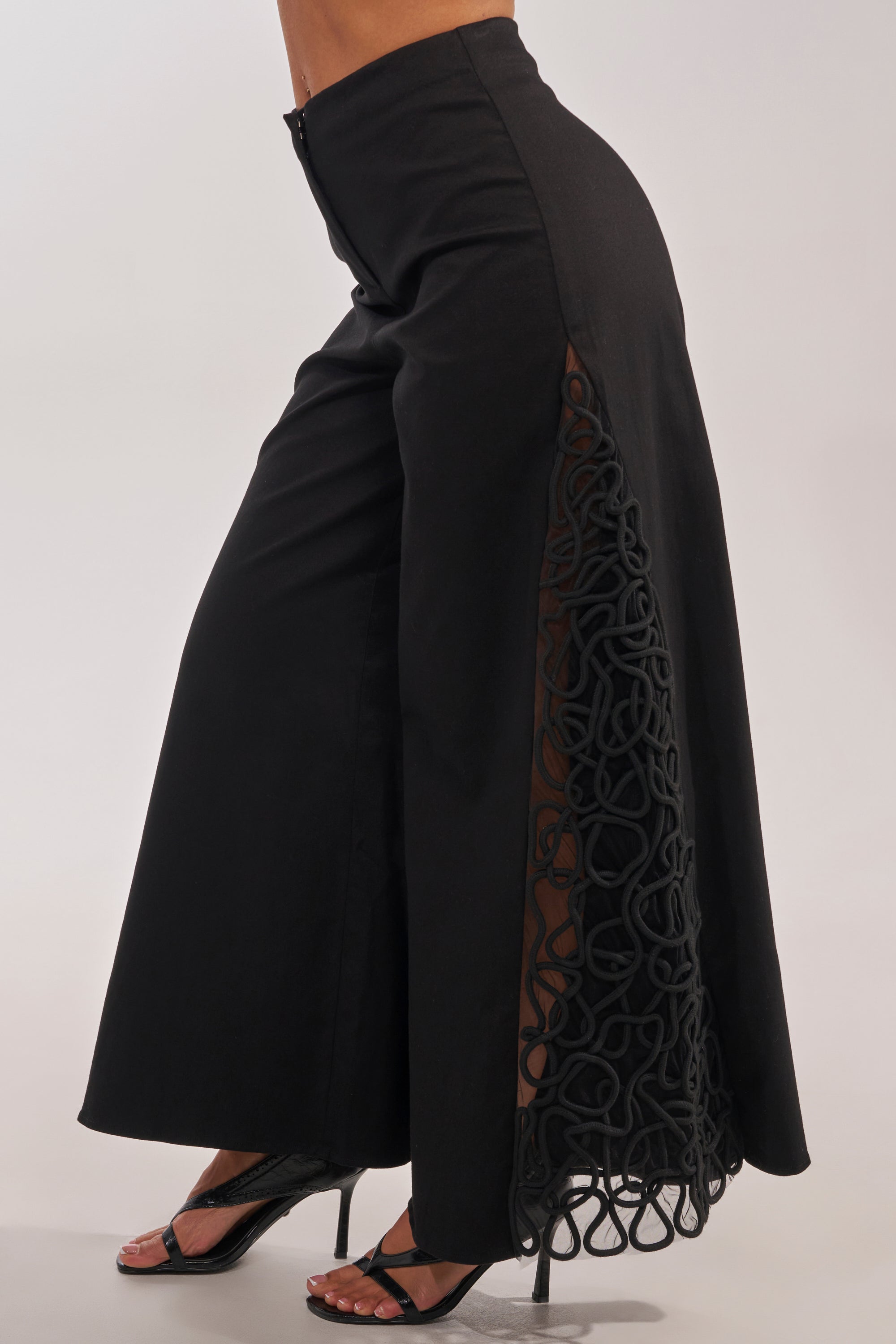 Someone wearing the ITS GIVING ROPE DETAIL TROUSER, featuring high-waisted wide-leg style and rope accents, paired with black heeled sandals—perfect for a formal occasion. 4