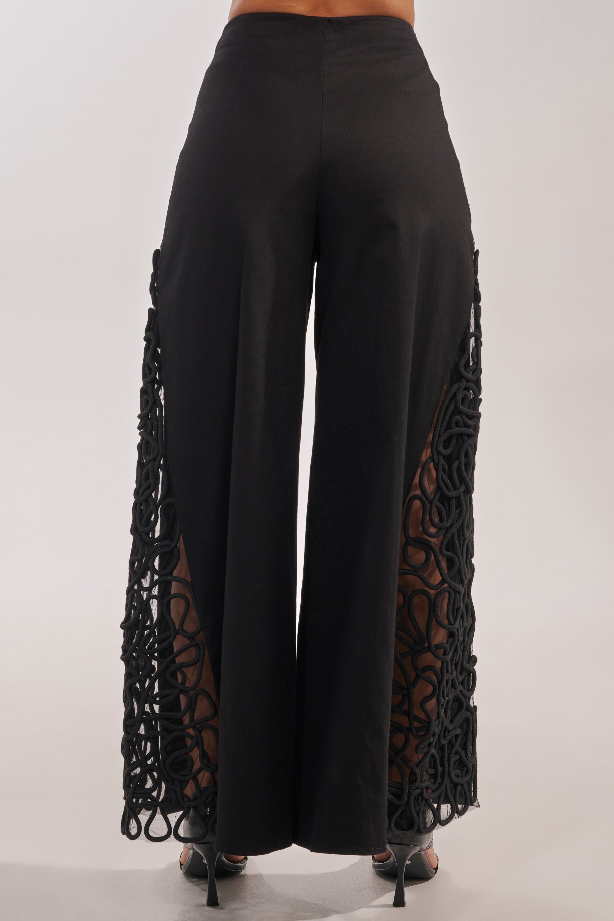 Wearing the ITS GIVING ROPE DETAIL TROUSER—black high-waisted wide-leg pants with rope detailing—styled with black high-heeled sandals against a neutral backdrop. Ideal for formal occasions. 5