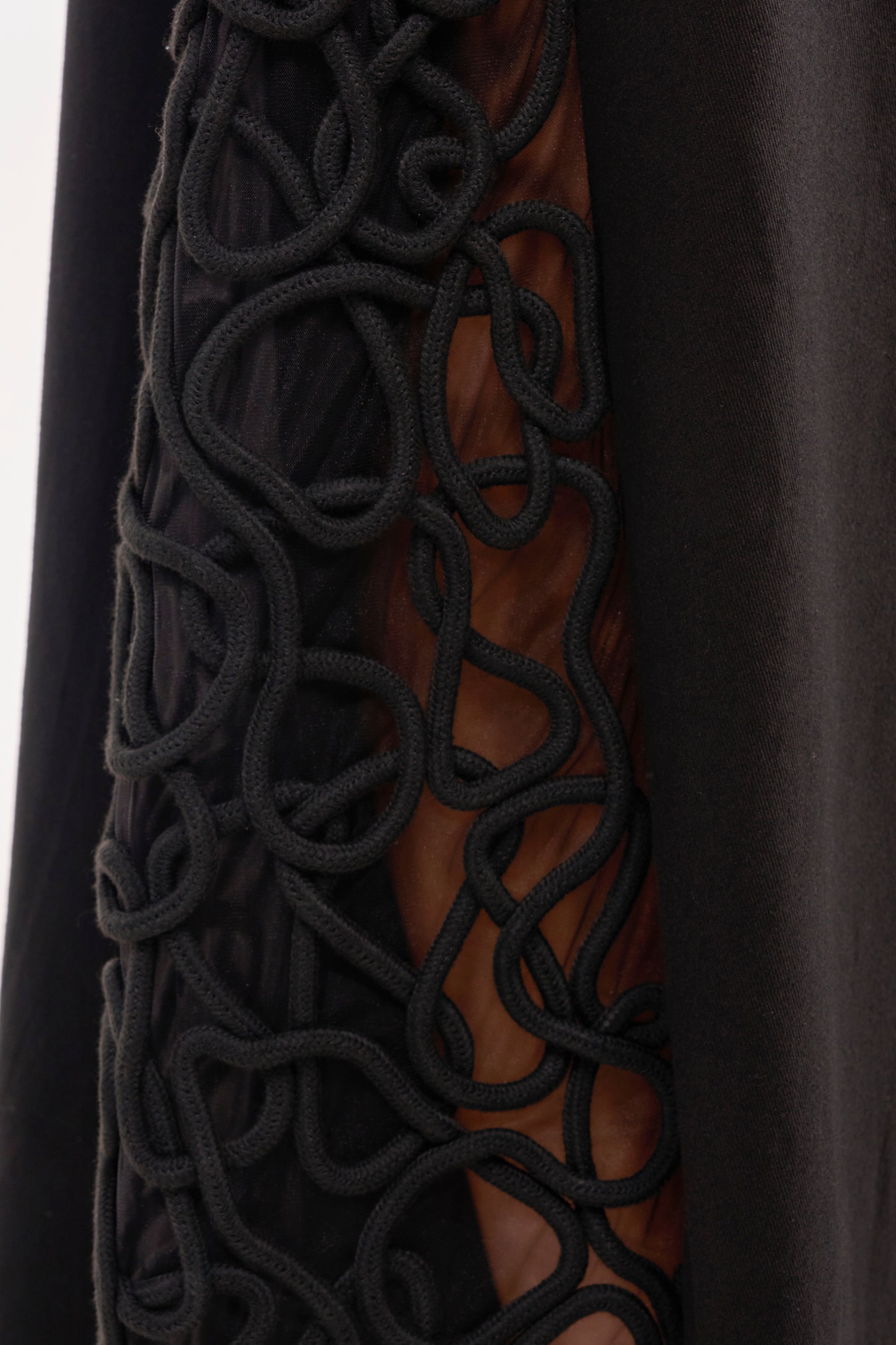 Close-up of ITS GIVING ROPE DETAIL TROUSER in black fabric with a sheer panel and decorative rope detail, subtly revealing skin beneath—an elegant statement for evening occasions. 7