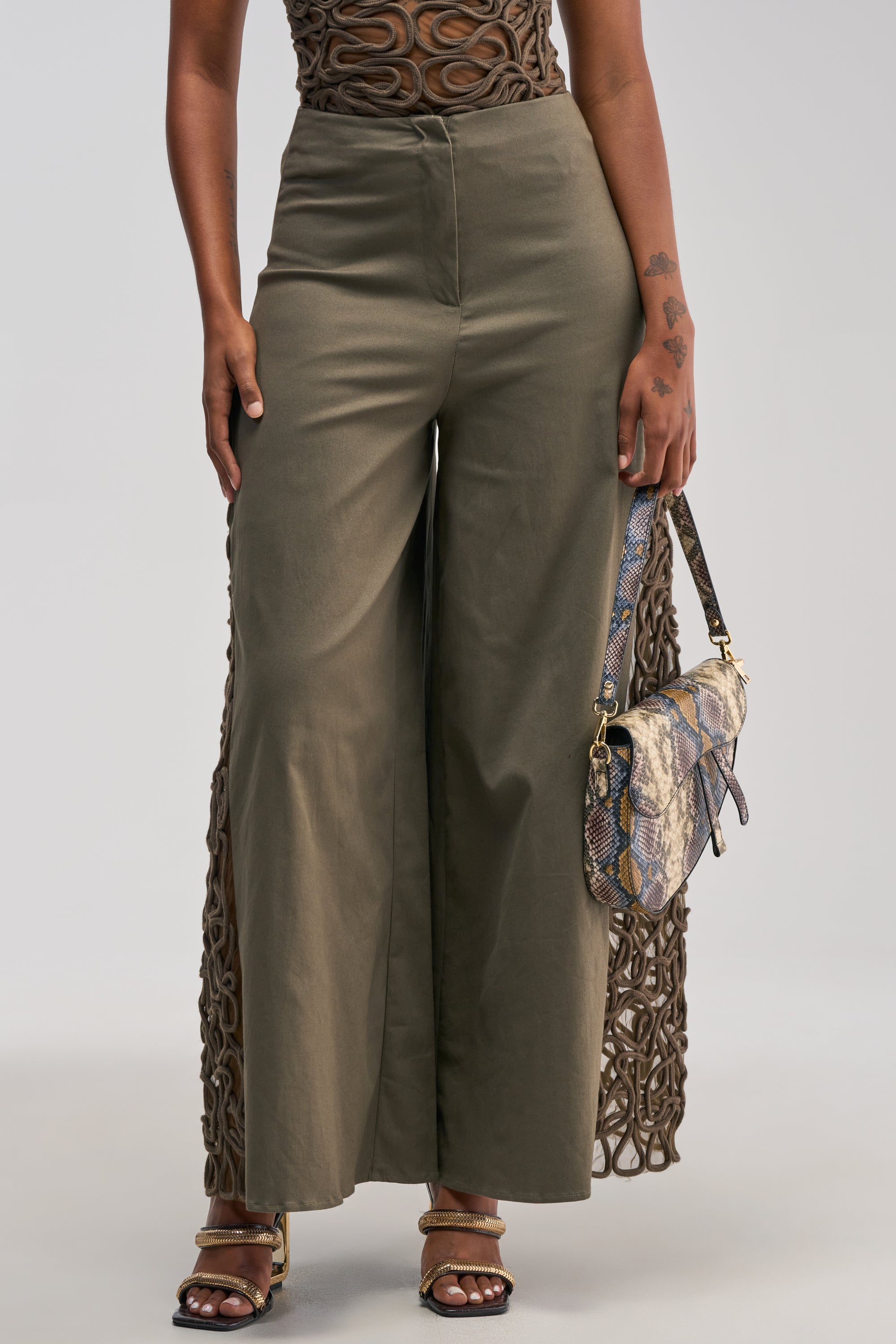A person wearing the ITS GIVING ROPE DETAIL TROUSER IN OLIVE styled in a business-casual way, paired with a brown textured top, heeled sandals, and holding a snakeskin-patterned handbag.