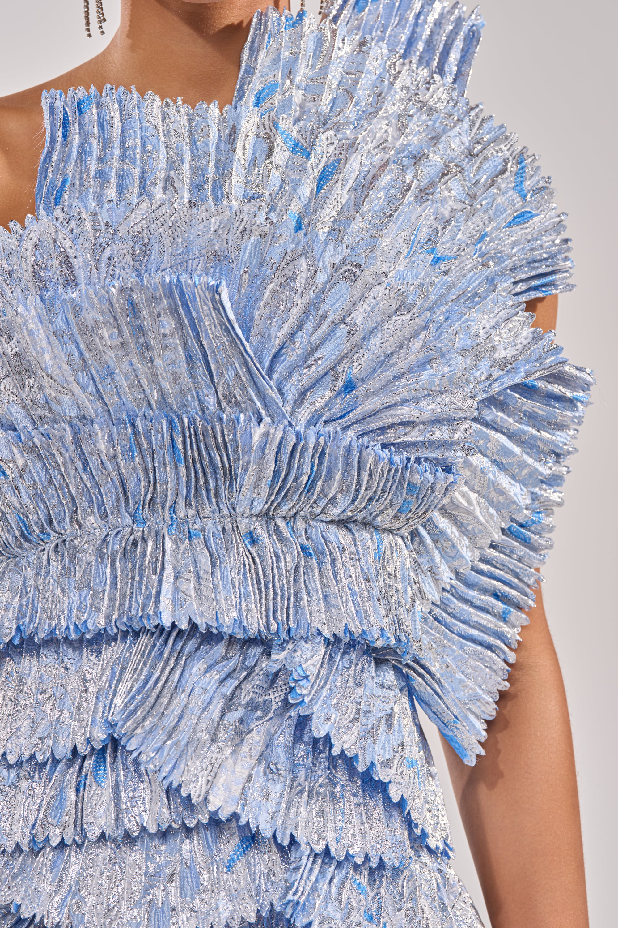 Close-up of the LUST FOR LIFE ASYMMETRICAL BROCADE MIDI DRESS IN BLUE, featuring textured fabric with layered ruffles and metallic blue-silver details. A one-shoulder neckline and sculptural fan-like effect add dramatic flair. 5