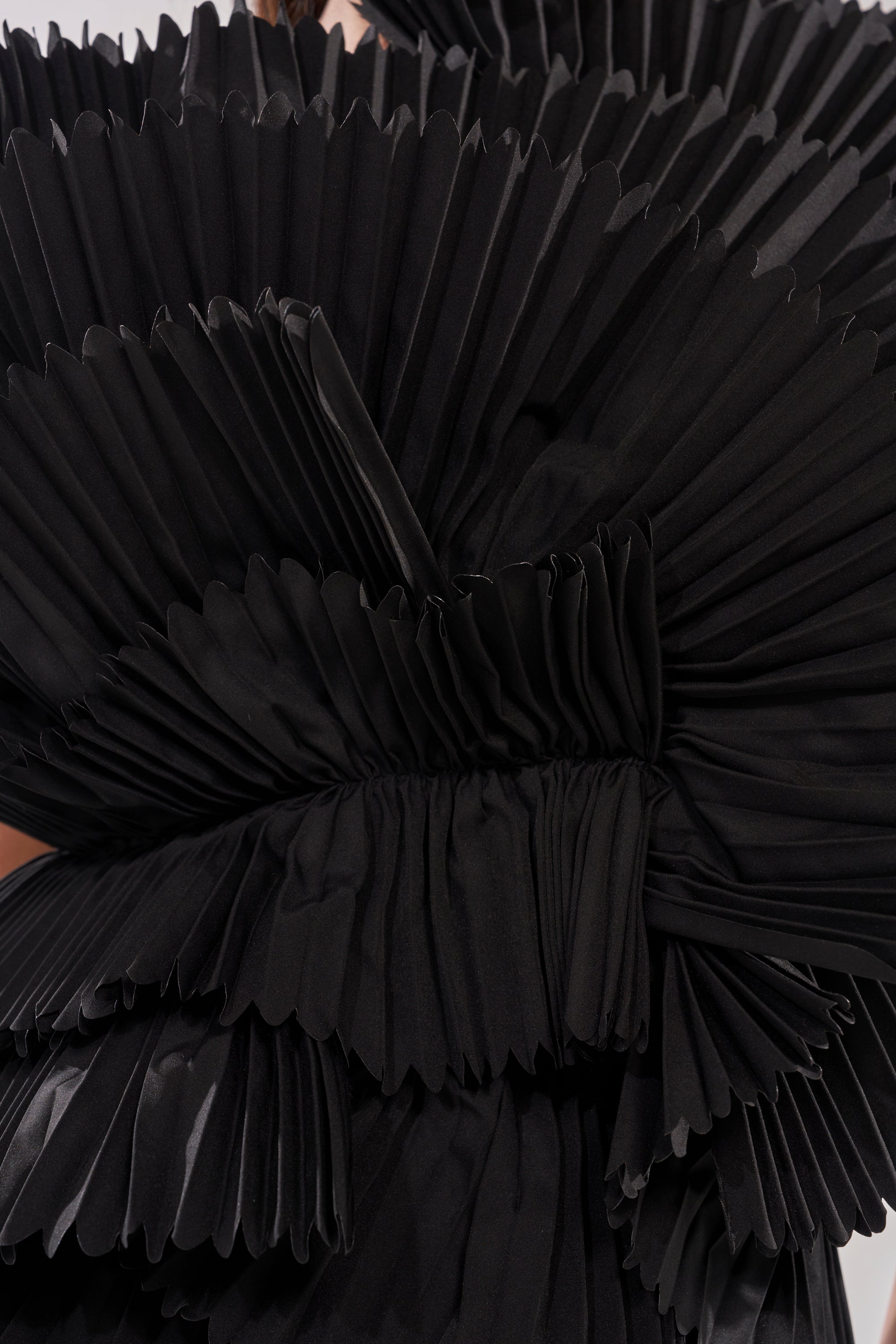 Close-up of the LUXURIOUS ASYMMETRICAL TOP IN BLACK, featuring dramatic ruffled shoulders and pleated fabric arranged in layered, fan-like shapes for a sculptural, textured look. 7