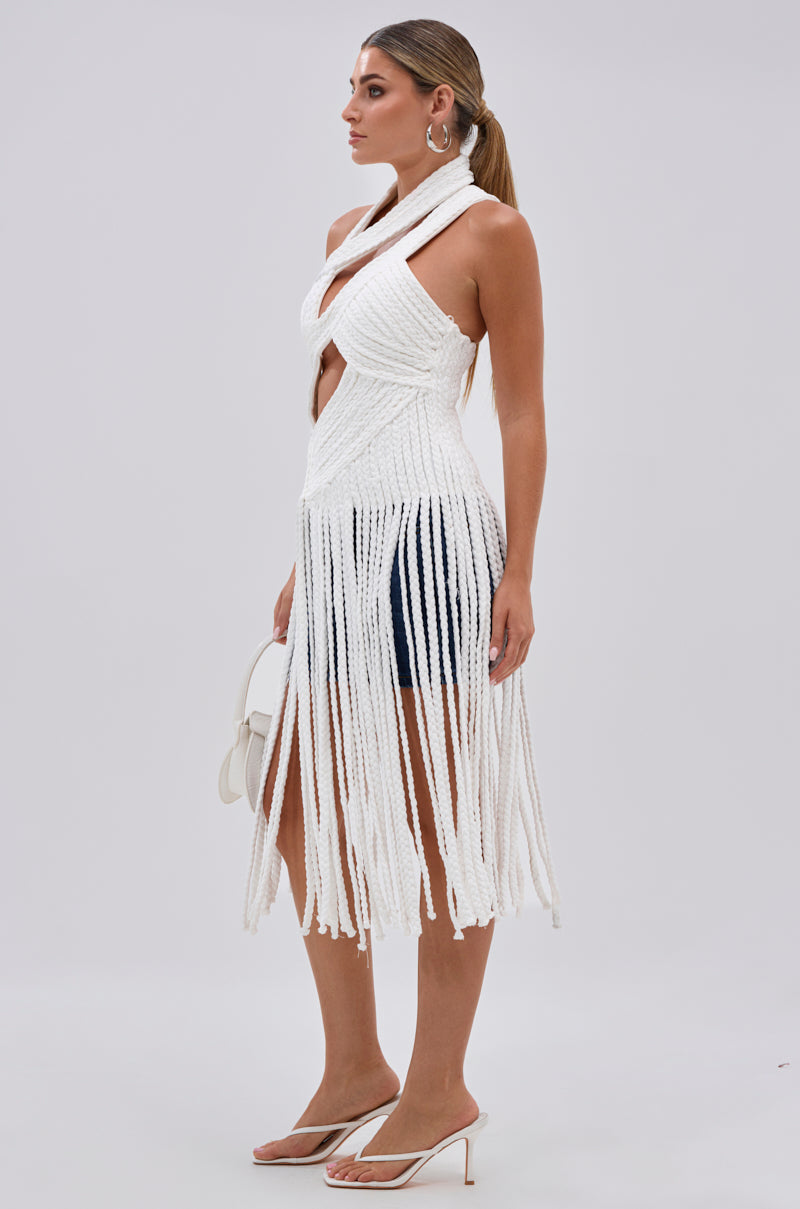 A woman in profile wears the CRAZY BUT THE SAME ROPE BLOUSE with a fringe hem over black shorts, accessorized with a small white handbag, hoop earrings, heeled sandals, and her hair in a ponytail.