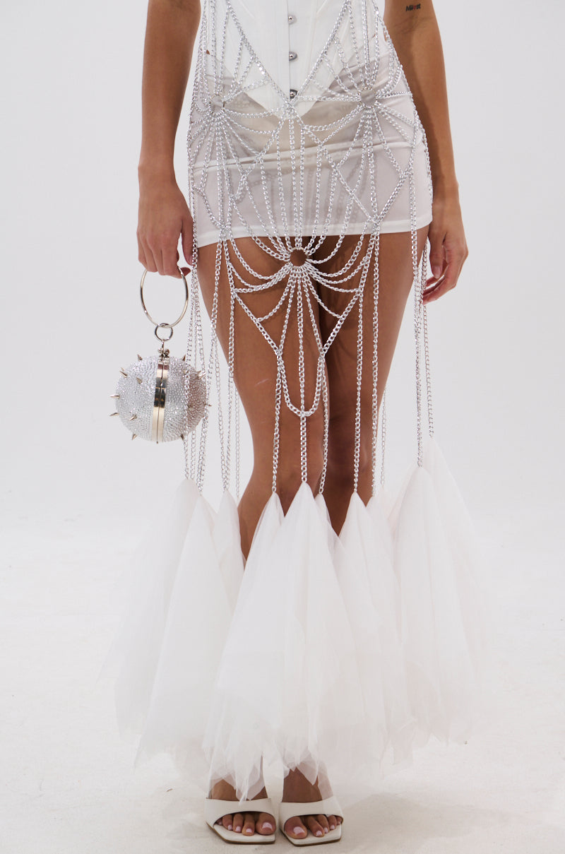 Wearing the BEST DRESSED BLOUSE WITH TULLE, featuring sparkling chain details, sheer panels, dramatic tulle accents by the ankles, and a corset-style design. Styled with a spiked silver handbag and white high-heeled sandals. 6