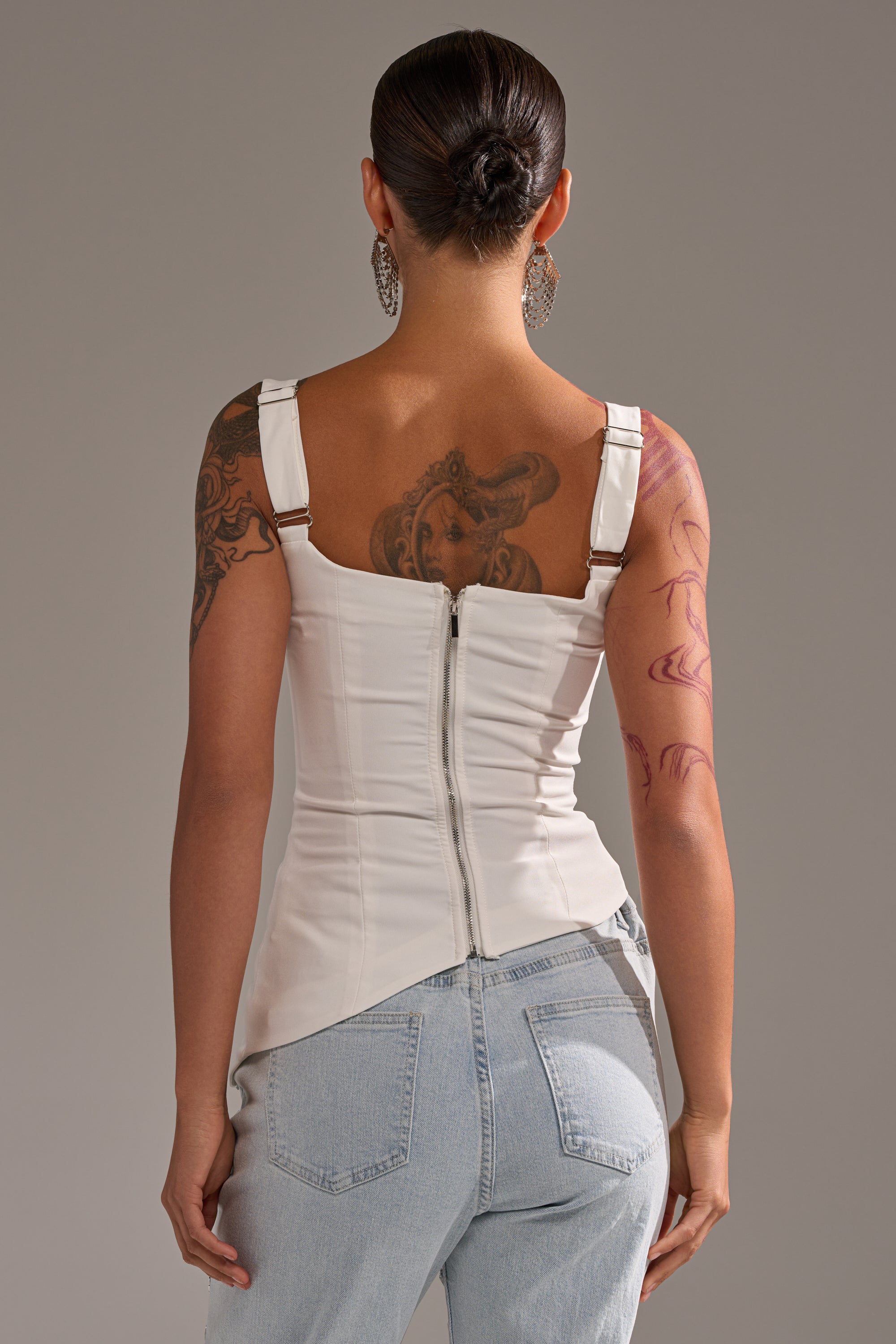 A tattooed person is shown from behind wearing the PLAIN JANE SLEEVELESS BLOUSE in white and light blue jeans. Their hair is styled in a low bun. 4