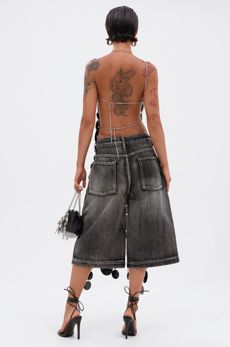 A person with short dark hair and tattoos is shown from the back wearing the GLAMOROUS CHAIN DETAIL HALTER TOP, wide-leg faded black denim culottes, lace-up high heel sandals, and holding a small handbag.