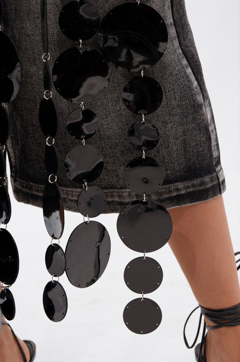 A close-up shows a person wearing a faded black denim skirt with shiny, oversized black discs and the GLAMOROUS CHAIN DETAIL HALTER TOP. Their legs and strappy black sandals are partially visible.