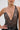 A woman wears the CHAINED DOWN HALTER NECK BLOUSE, featuring metallic mesh fabric, a deep neckline, and silver rings on one shoulder. She pairs it with large hoop earrings; her hand is on her hip and her face is partially visible.