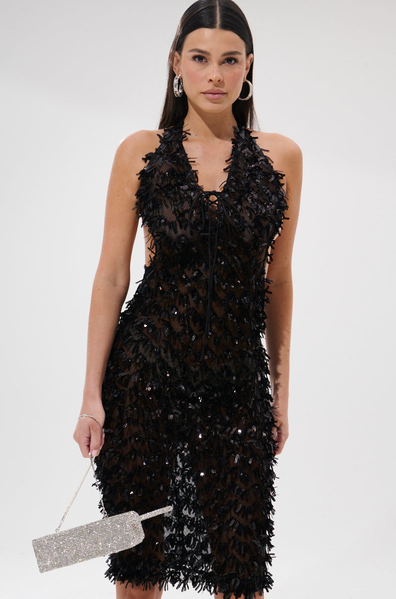 A woman wears the LENNOX SEQUIN MESH MIDI DRESS with a plunging neckline and sparkly silver clutch. Her straight dark hair, hoop earrings, and confident expression stand out against a plain white background.