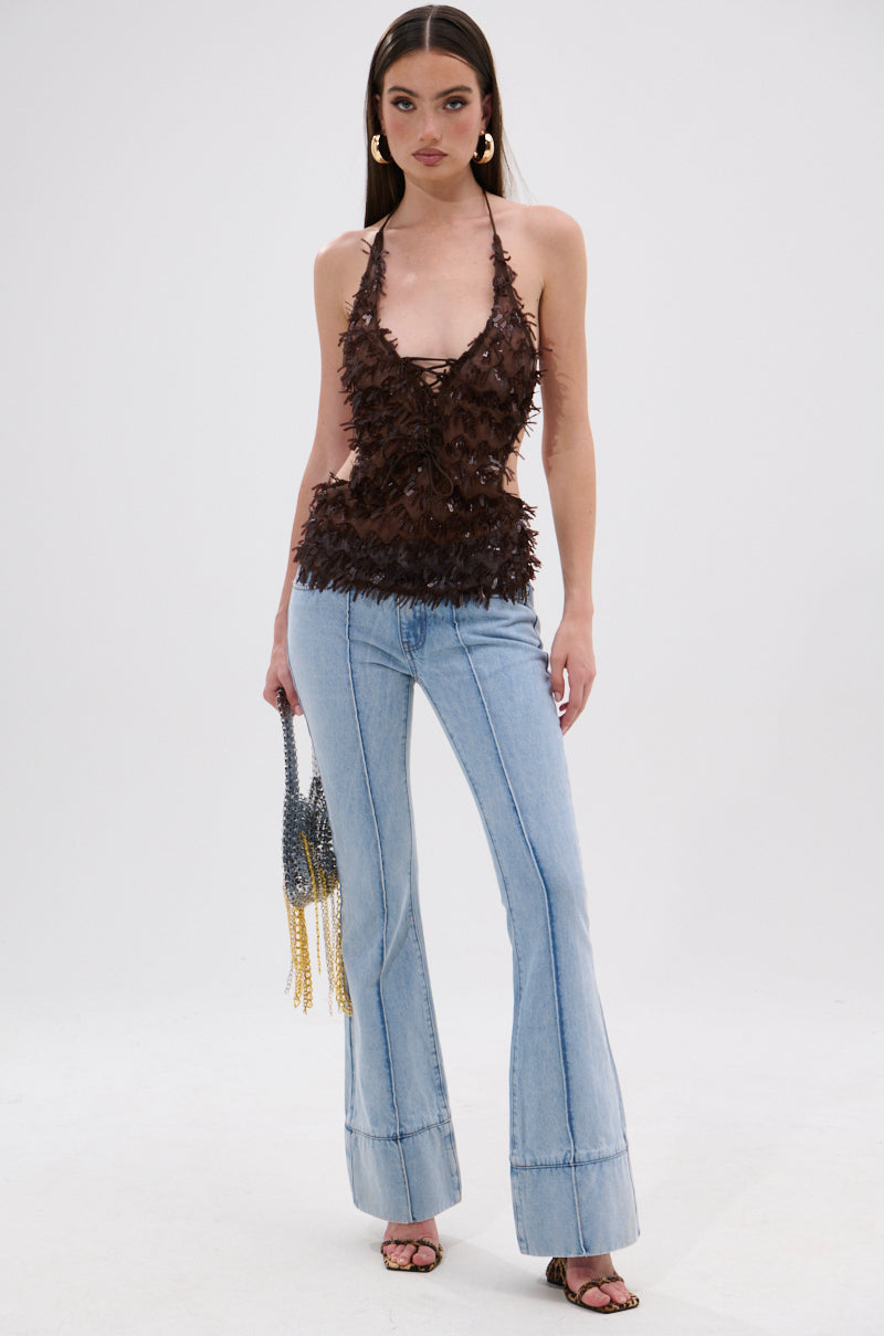 A woman wears the SEQUIN FRINGE QUEEN HALTER NECK BLOUSE, a sleeveless brown textured top, paired with light blue flared jeans, hoop earrings, a beaded handbag, and heeled sandals, posing against a plain white background. 5