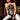 A woman with long dark hair wears the LETS GET FUNKY BEADED TOP and black-and-white tie-dye pants, sitting confidently on a wooden surface in a warmly lit, stylish indoor space.