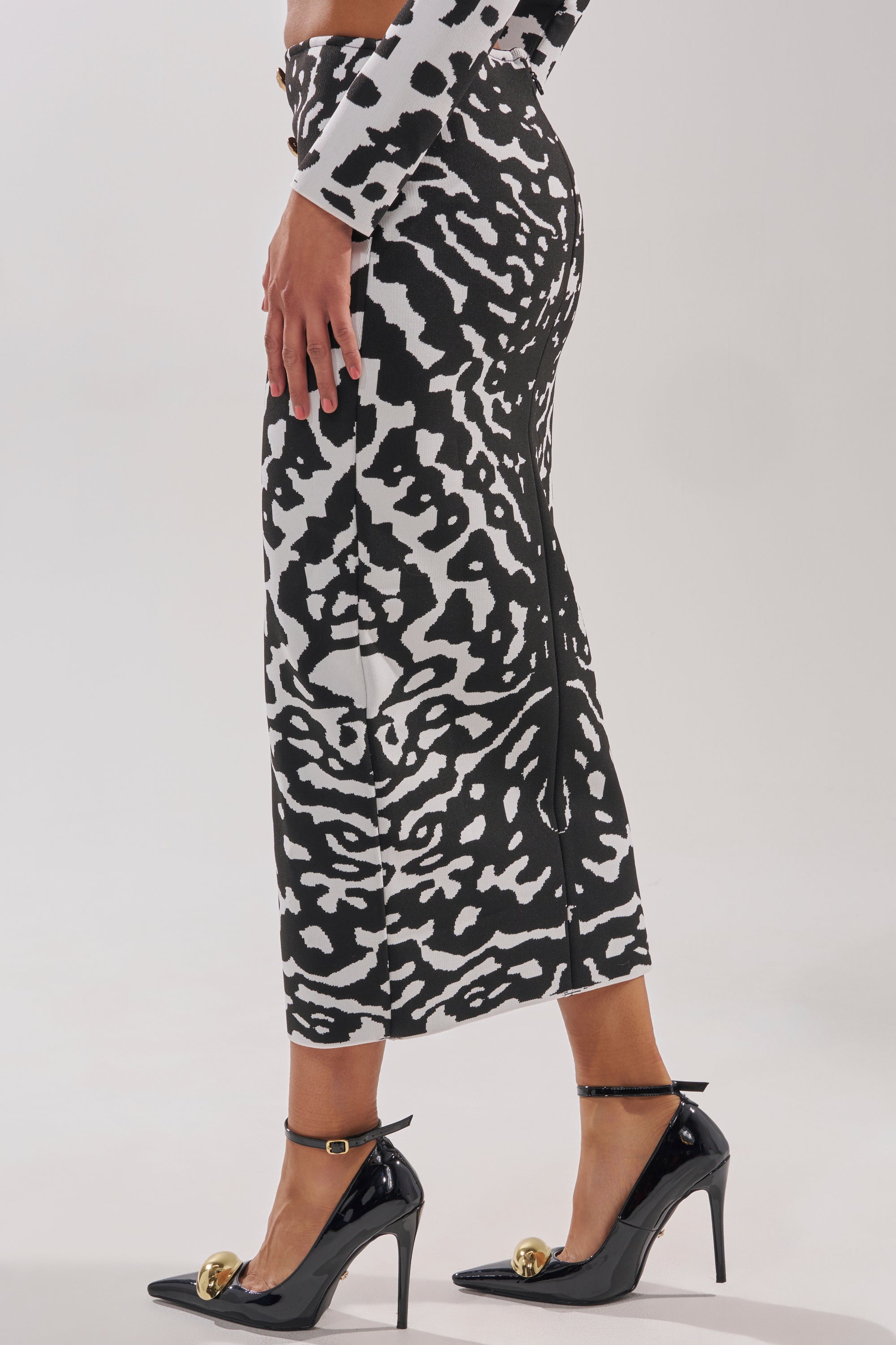 A person wearing the BEST DRESSED MAXI SKIRT in a black and white abstract print with a matching long-sleeve top and gold-embellished black heels, posed side-on against a plain background.