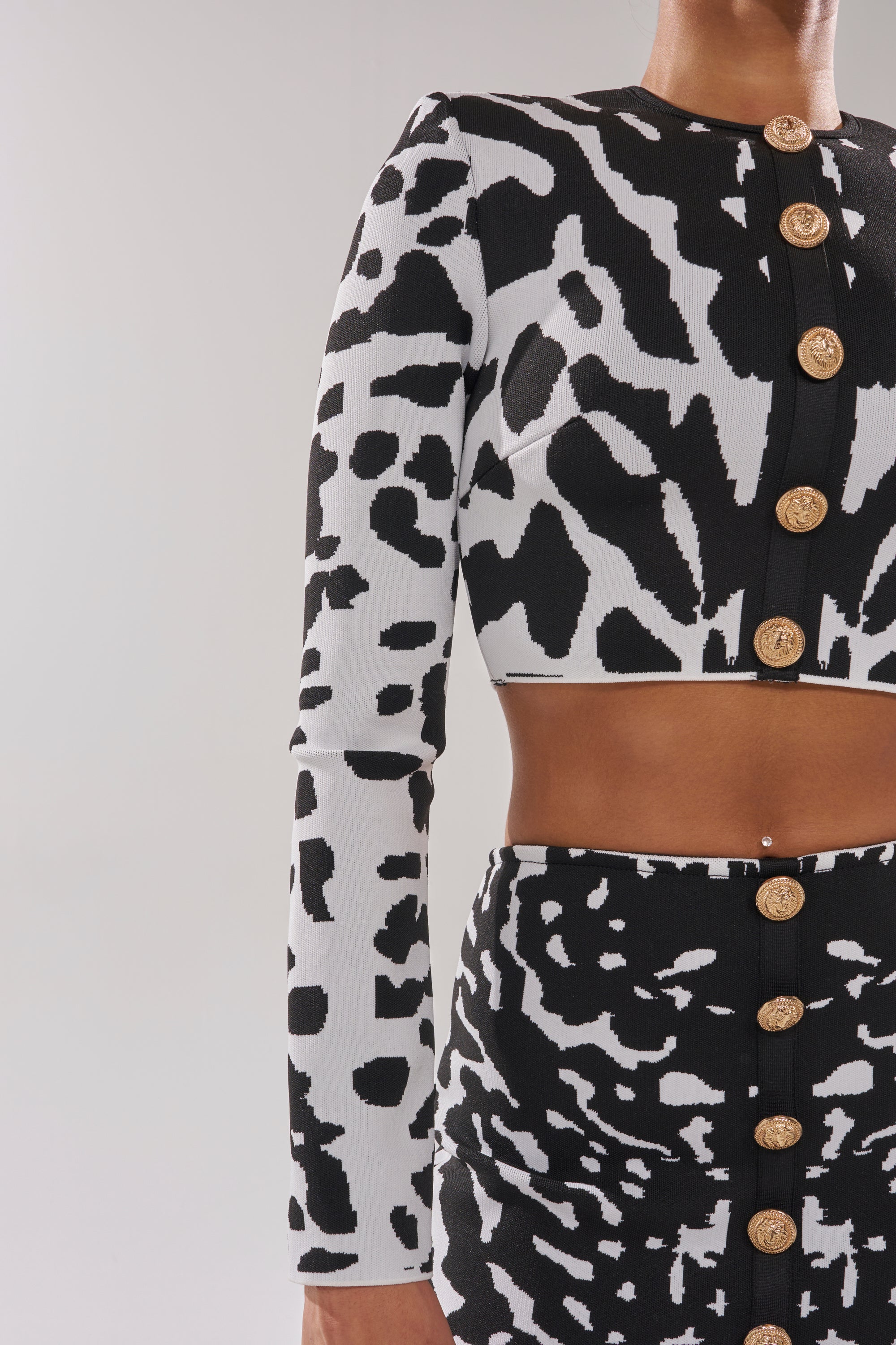 A model wears the BEST DRESSED CARDIGAN over a black and white animal print crop top and matching high-waisted skirt with large gold buttons, shown from shoulders to thighs against a plain background. 7