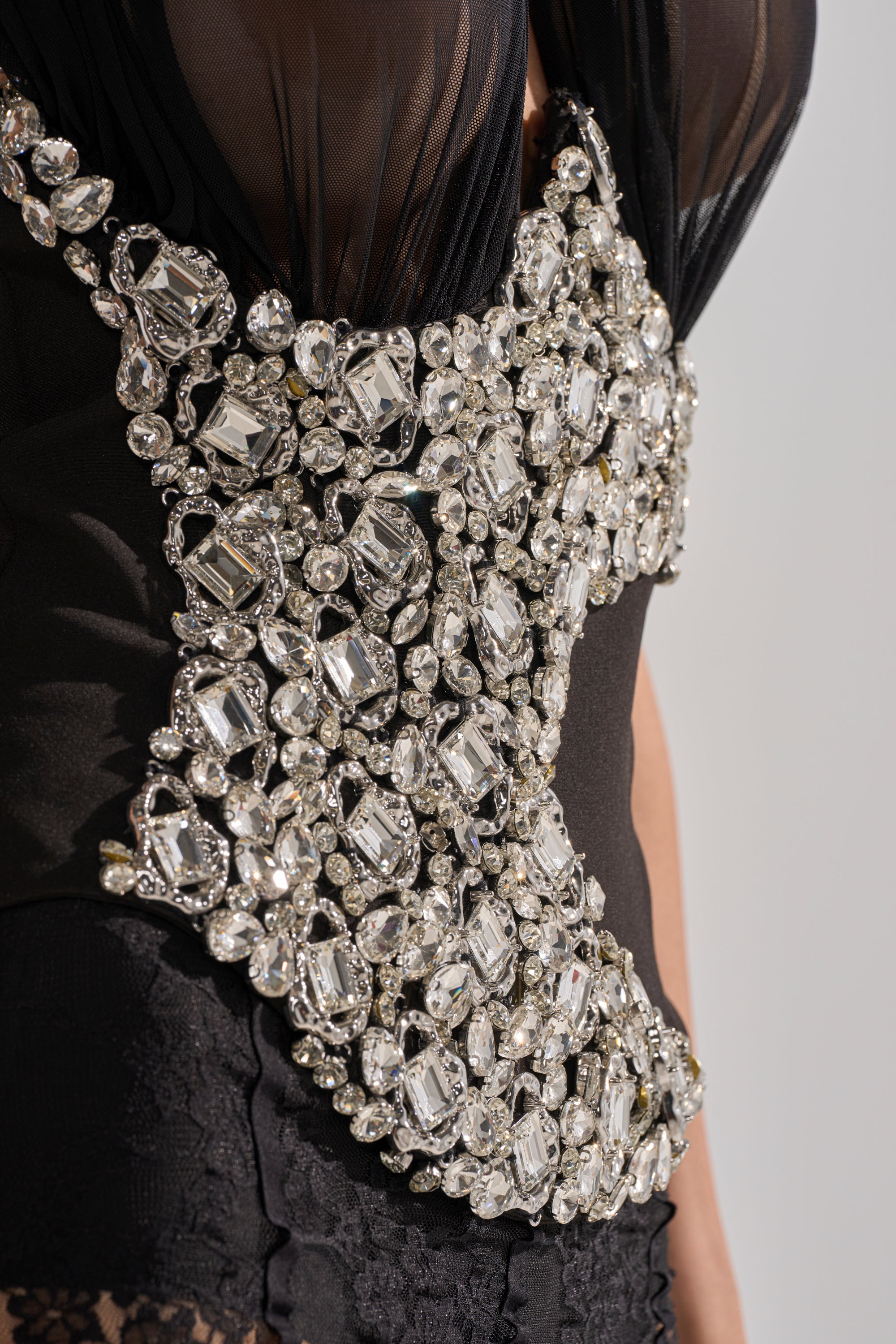 A close-up of a person wearing the JEWELED CROSSOVER HALTER NECK CORSET, featuring black mesh embellished with large, sparkling rhinestones in an intricate pattern across the bodice. 7