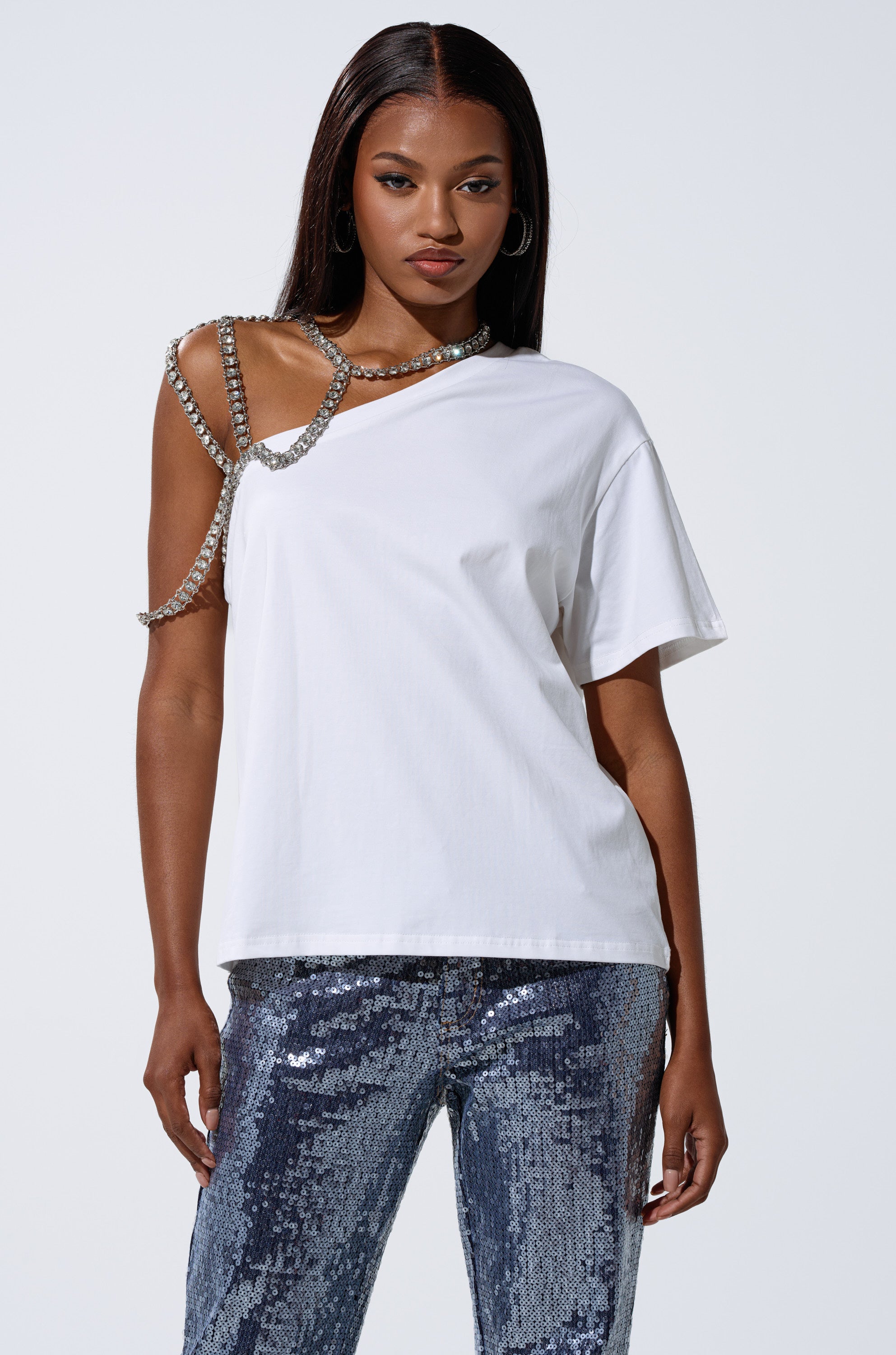 A woman wears the DANCING STAR OVERSIZED TEE with a rhinestone harness over one shoulder and sequined silver pants, standing against a plain background. 1