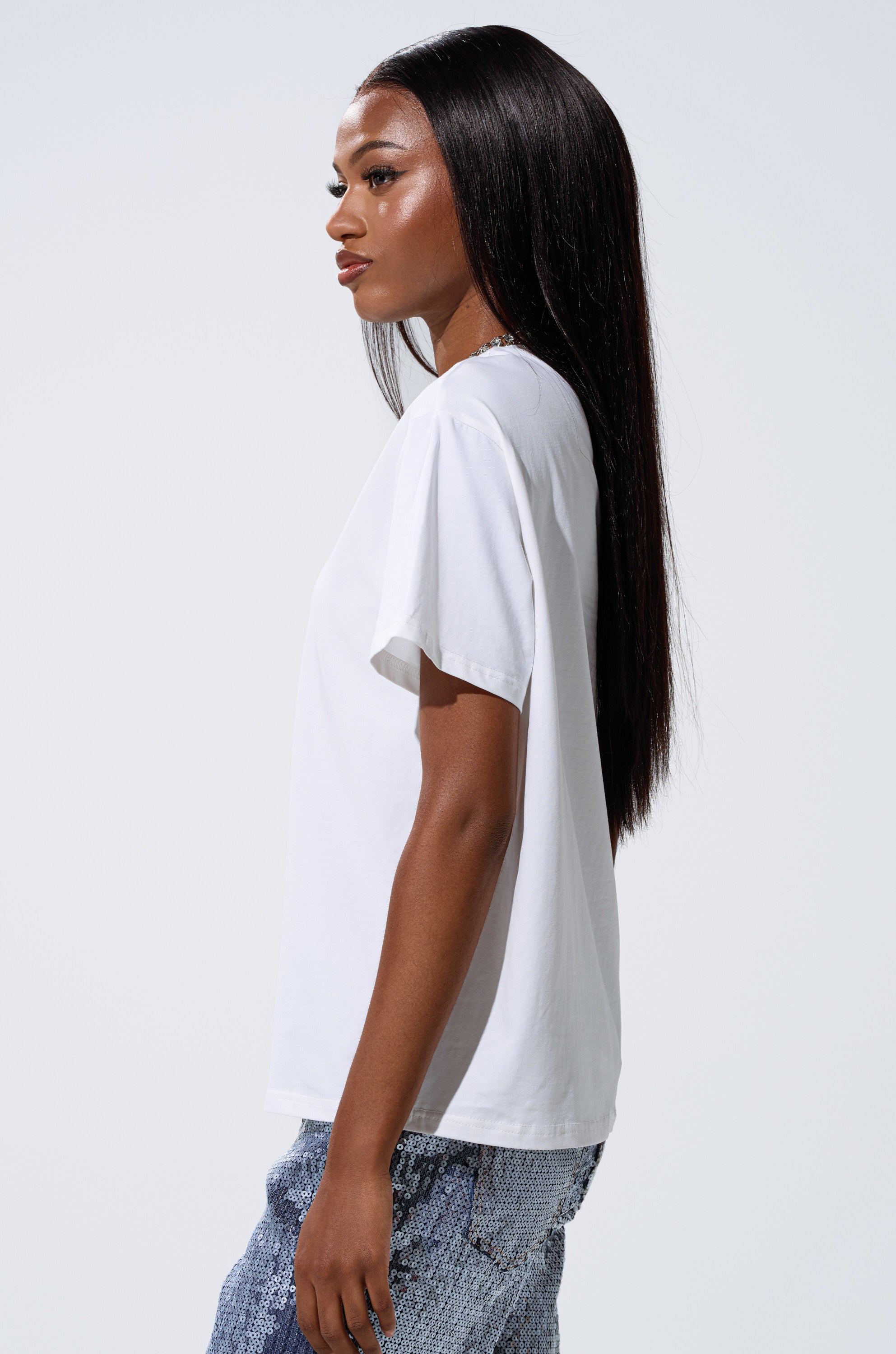 A woman with long straight hair stands in profile against a plain light background, wearing blue jeans and the DANCING STAR OVERSIZED TEE. 3