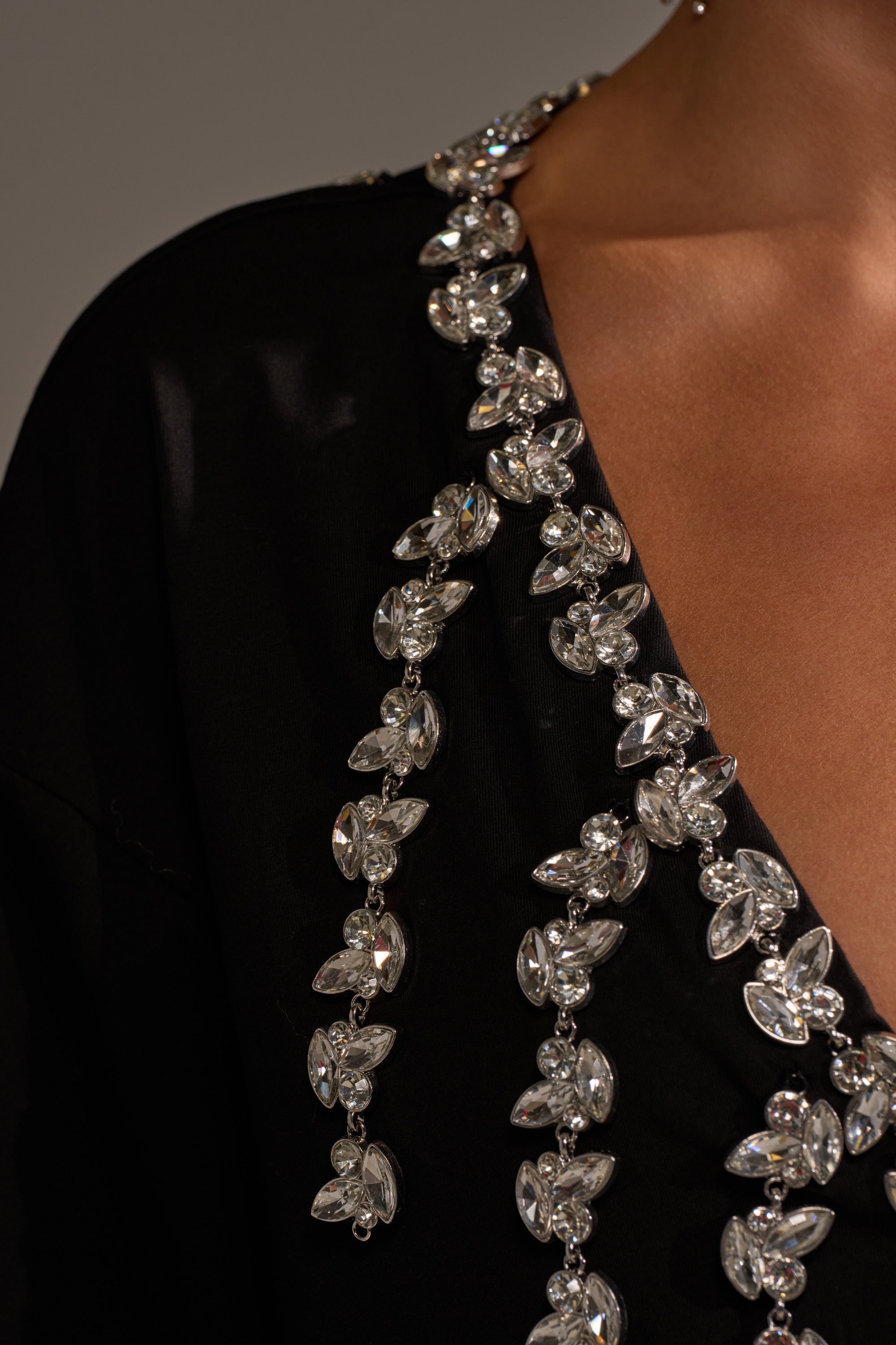 A close-up of a person wearing the RHINESTONE QUEEN OVERSIZED TEE, featuring a plunging V-neckline with sparkling rhinestone embellishments arranged in a decorative edge pattern.