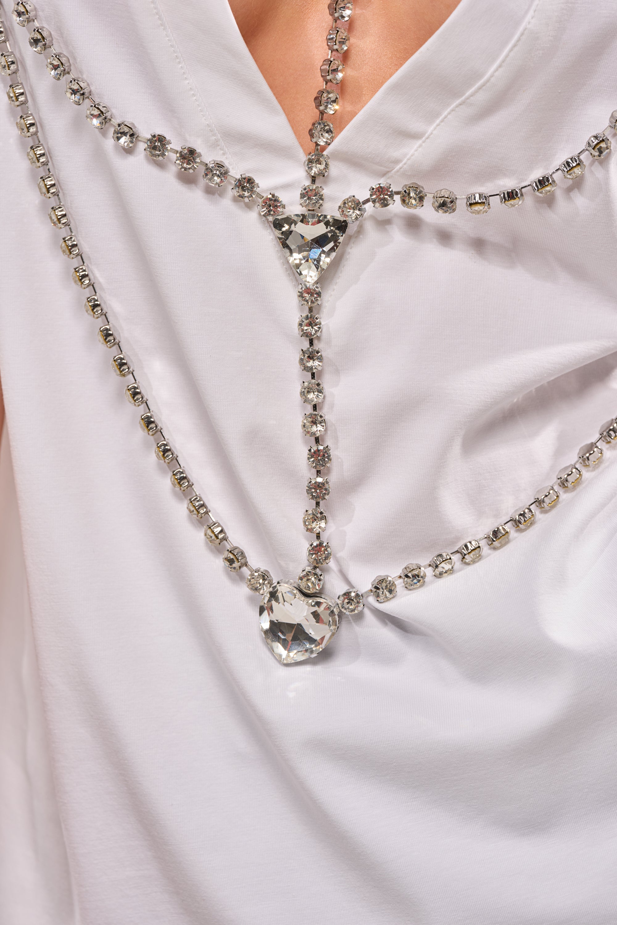 Close-up of the DIAMONDS DANCING RHINESTONE DETAIL TEE, featuring a decorative crystal chain with large clear triangular and heart-shaped gems draped elegantly across the back. 10