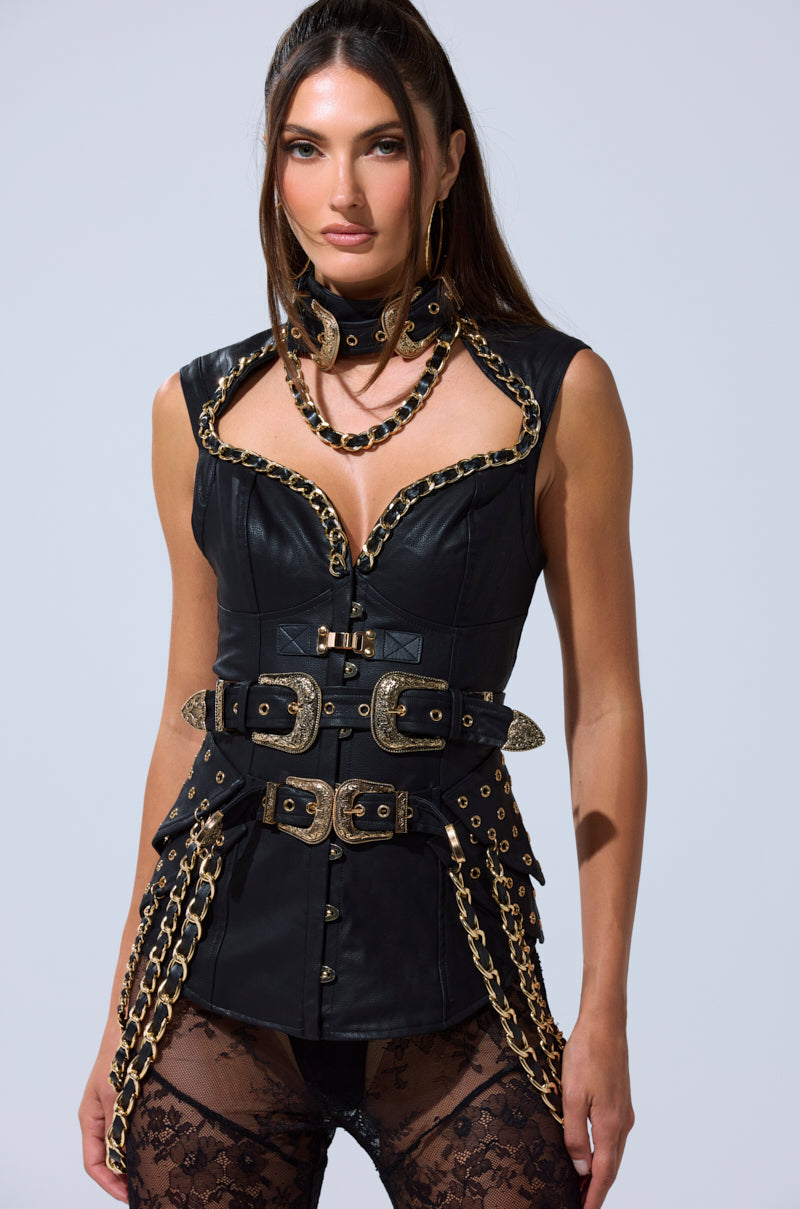 A woman models the LETS GO TO THE RODEO BLOUSE, a black vegan leather corset-style top with gold chain details, paired with double-buckled belts, a lace choker, hoop earrings, and sheer black lace stockings against a plain light background. 4
