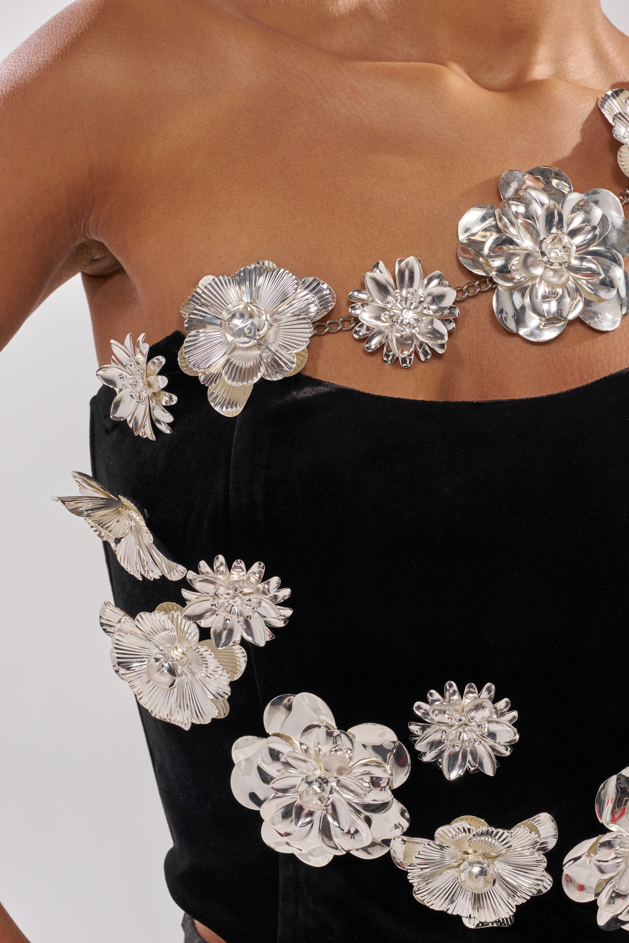 A close-up of a person wearing the BLINGING OUT CORSET, a black strapless corset featuring shiny silver metallic flower and butterfly decorations on the front and neckline. 9