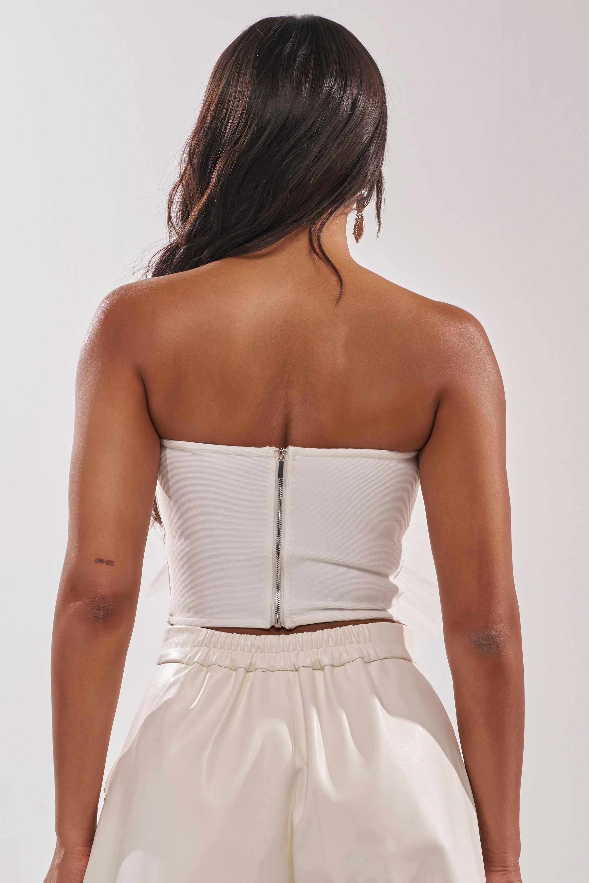 A woman with long dark hair is shown from behind wearing the ALL DIFFERENT WAYS CORSET, a white zip-up top, paired with loose white pants. 5