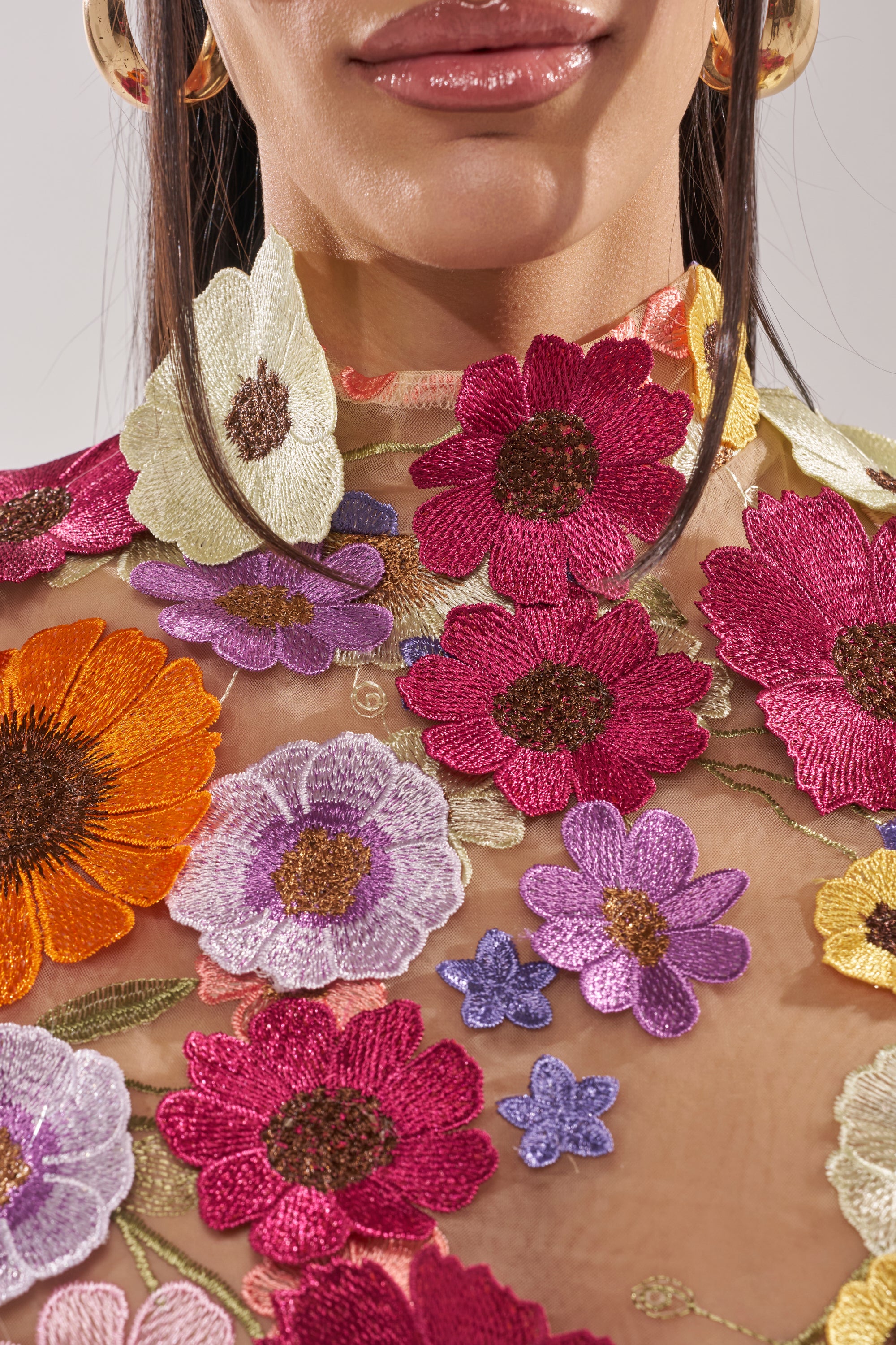 A close-up of a woman's lower face and neck in the WHERE THIS FLOWER BLOOMS MESH TOP, featuring sheer fabric densely adorned with colorful 3D floral embroidery in purple, pink, orange, and white. 6