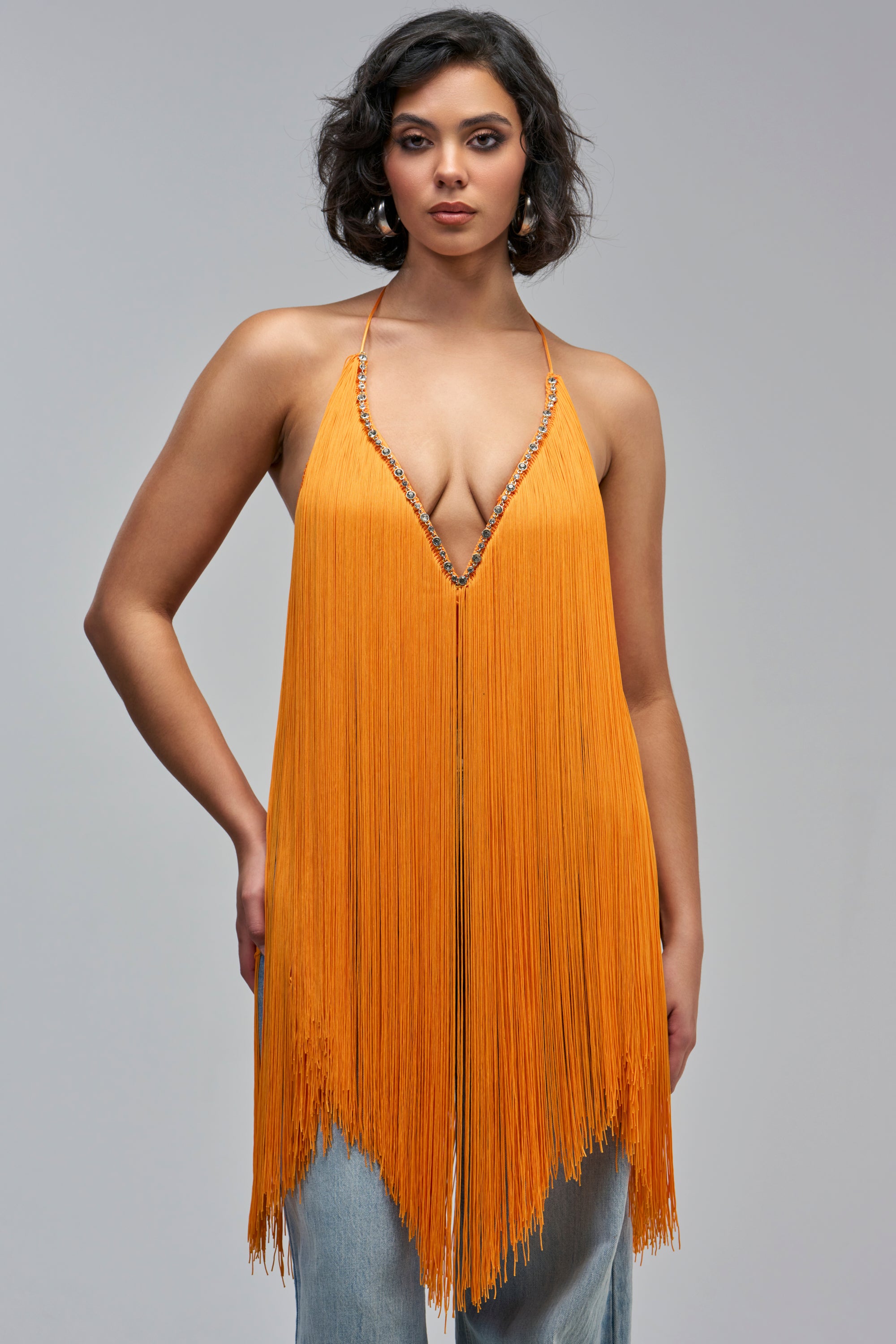 The SWEPT AWAY FRINGE TOP IN MARIGOLD is a sleeveless top with a deep V-neckline, featuring decorative multicolored crystals and fringe detailing.