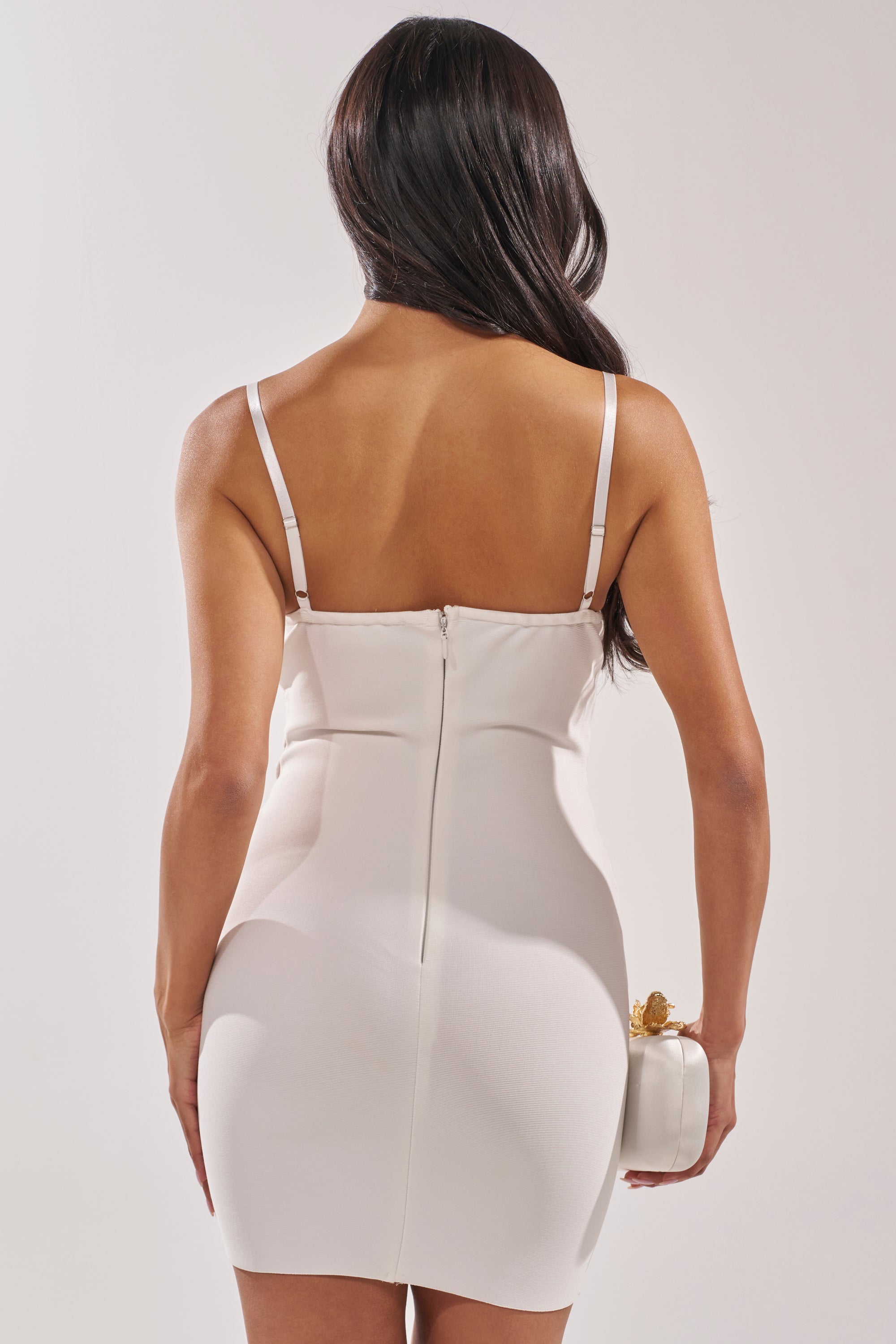 A woman with long dark hair, seen from behind, is wearing the ANYTHING BUT BASIC MINI DRESS in white and holding a small white clutch purse against a plain light background. 3