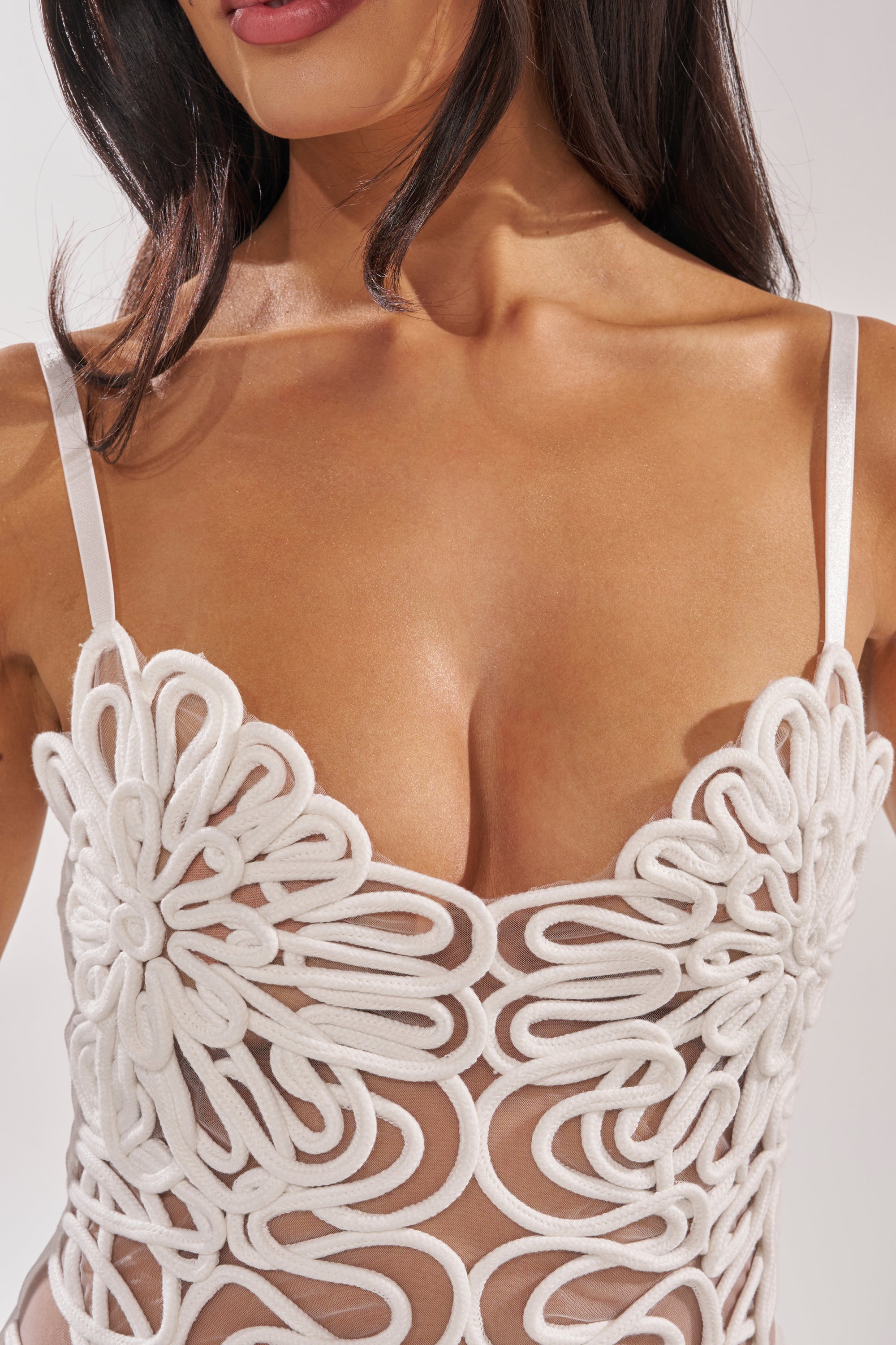 A woman wearing the ANYTHING BUT BASIC MINI DRESS, a white sheer mini dress with thin straps and intricate, swirling floral embroidery that evokes the detail of a bold 3D rope appliqué. 6