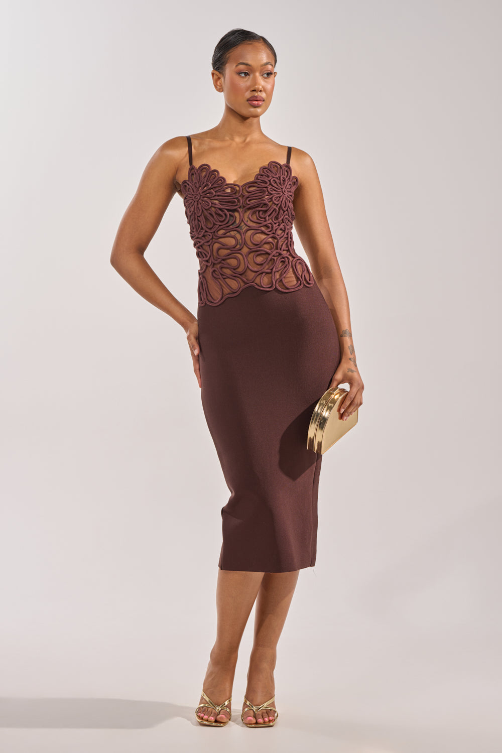 A woman in the ANYTHING BUT BASIC MAXI DRESS—maroon, fitted, with floral and rope details on the bodice, thin straps—pairs it with gold heels and a clutch against a light backdrop; an ideal look for formal occasions. 0