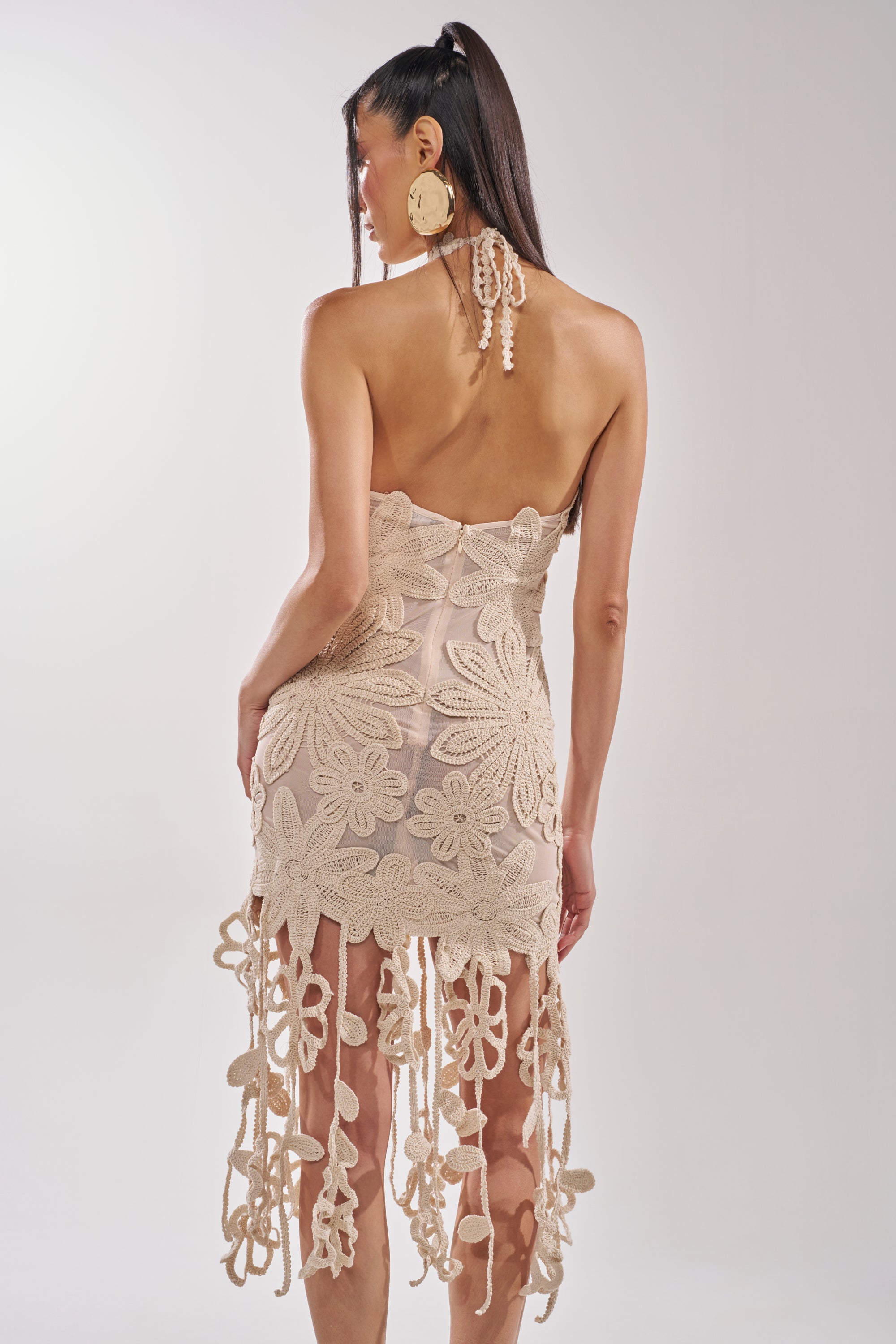 A woman with long dark hair models the CELINE FLORAL MIDI DRESS, an ivory crochet lace dress with large floral patterns, long tassels, and an open back—ideal for a bridal shower. 5