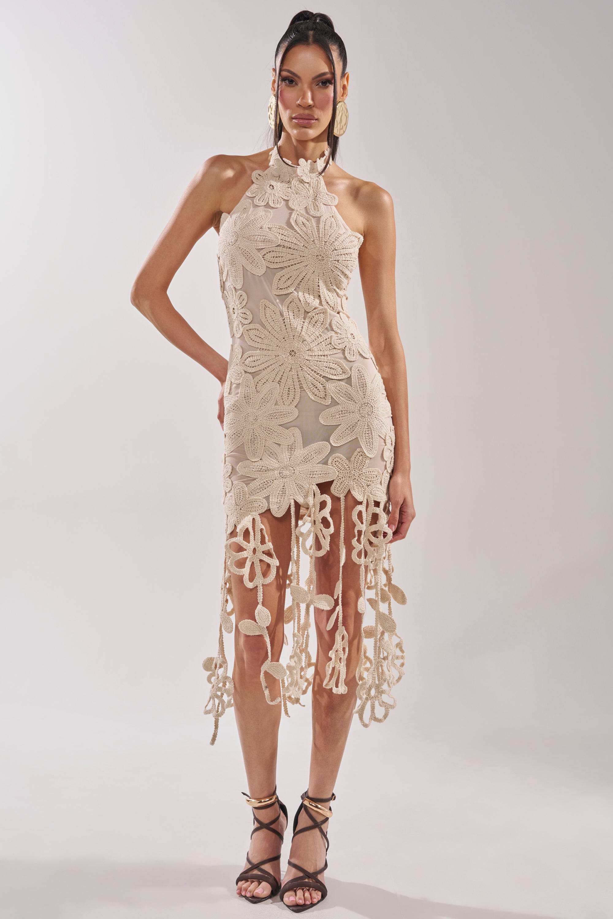 A woman poses against a plain background in the CELINE FLORAL MIDI DRESS—an ivory crochet lace midi with bold floral patterns and long fringe details, styled with black strappy heels for a chic bridal shower look. 8