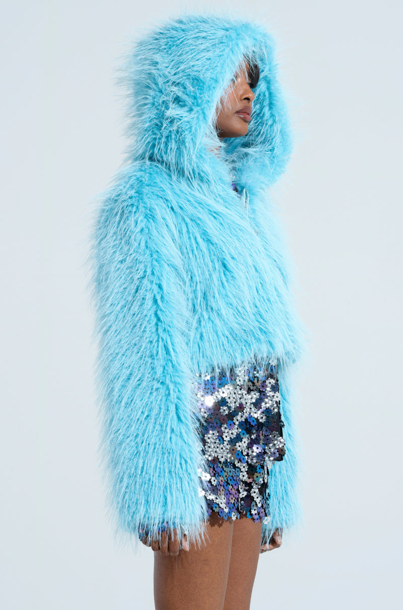 A person is wearing a KINGSTON FAUX FUR JACKET by AKIRA Label and a silver sequined skirt, standing in profile against a light-colored background.