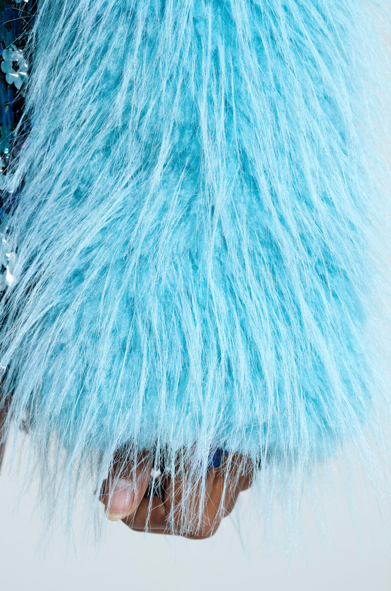 A close-up of a hand partially covered by the KINGSTON FAUX FUR JACKET reveals the soft texture of the fabric contrasted with blue-painted fingernails, set against an out-of-focus background.