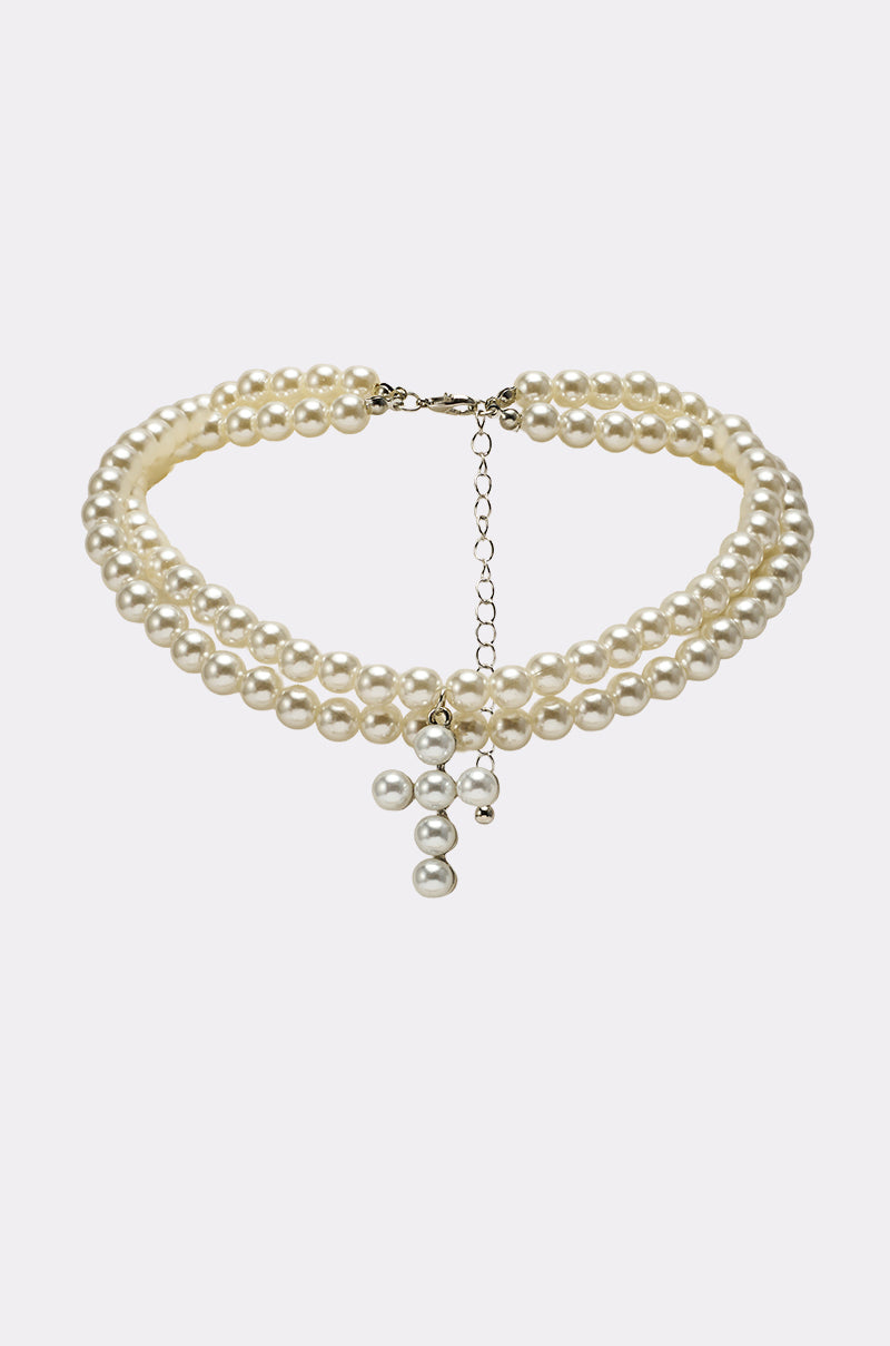 The PEARL DREAMING CROSS CHOKER features a double-stranded pearl design with an adjustable clasp and a central dangling cross-shaped pearl pendant. 0