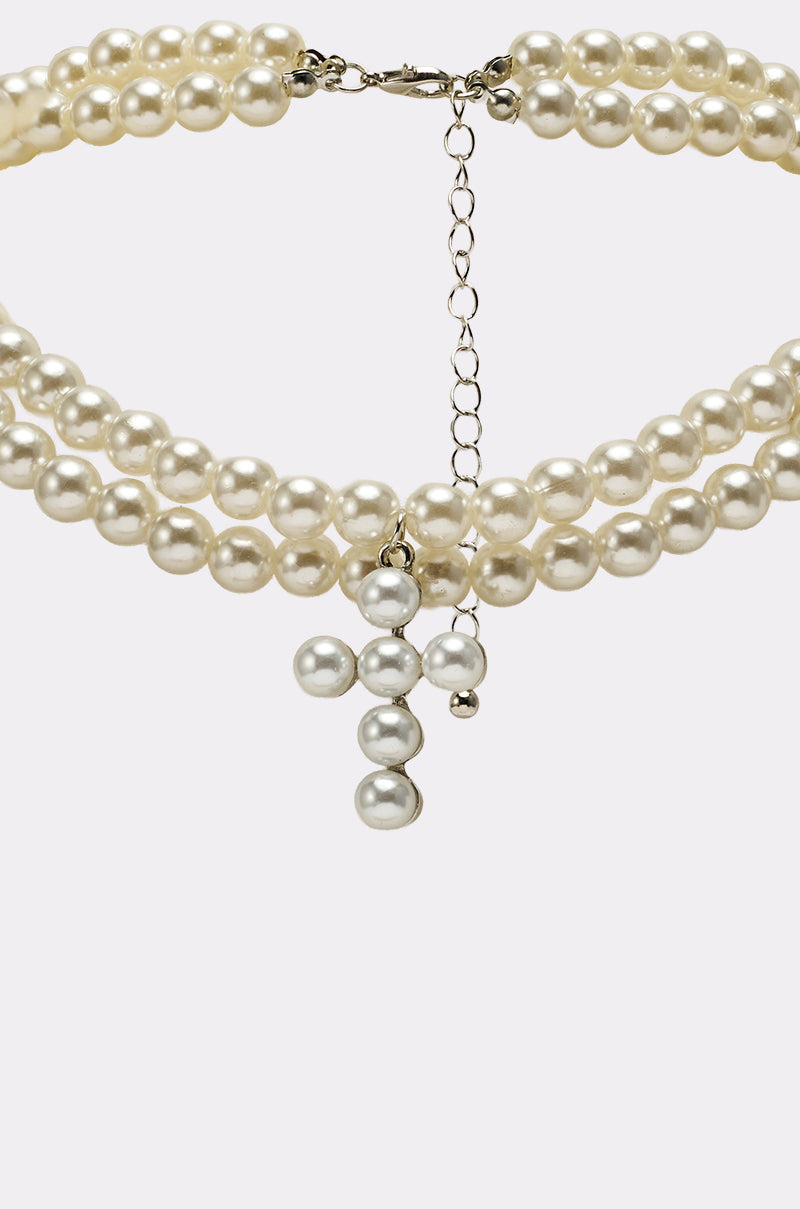 The PEARL DREAMING CROSS CHOKER is a layered three-strand pearl necklace with a hanging chain and bold pearl cross pendant, shown on a plain white background. 3